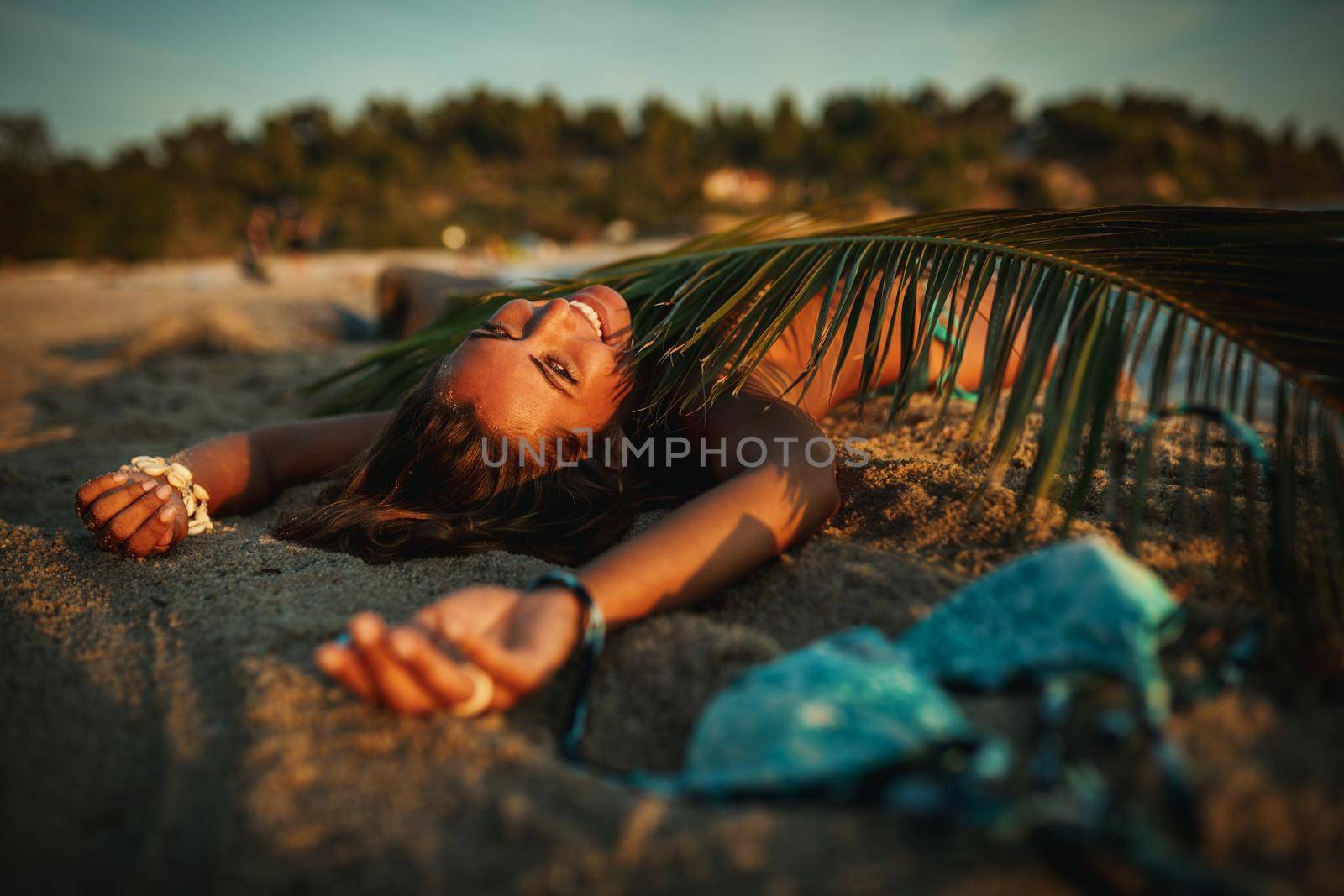 Shot of an attractive young woman is lying on the tropical sandy beach covered with palm tree leaf.