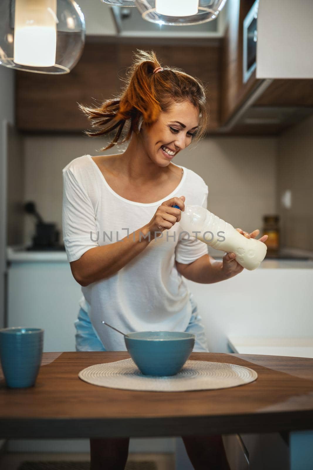 Beautiful young smiling cheerful woman is preparing her healthy breakfast in her kitchen, having fun and dancing.