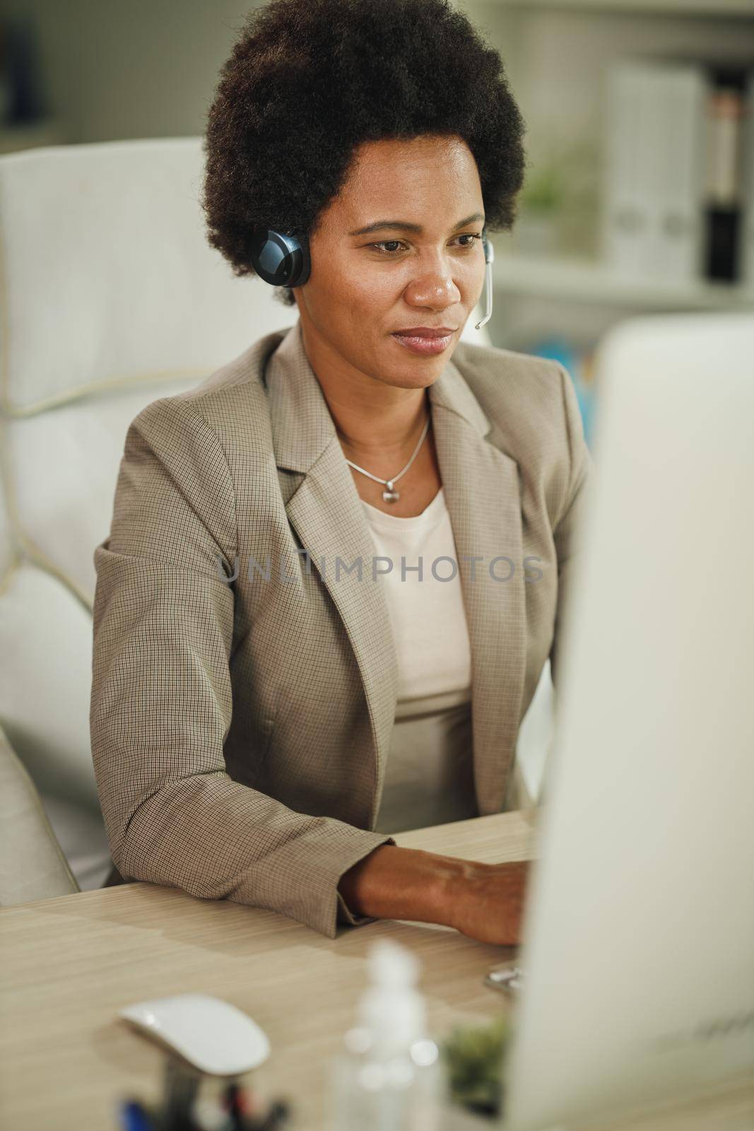 Shot of an African businesswoman wearing a headset while working on computer in her office during corona virus pandemic.
