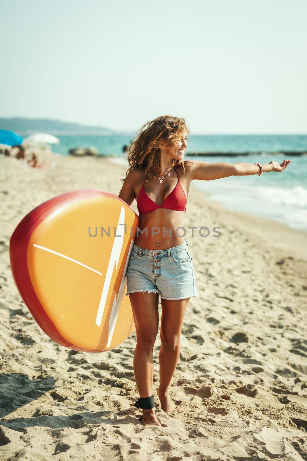 Beautiful young female surfer is walking on the beach with her surfboard.