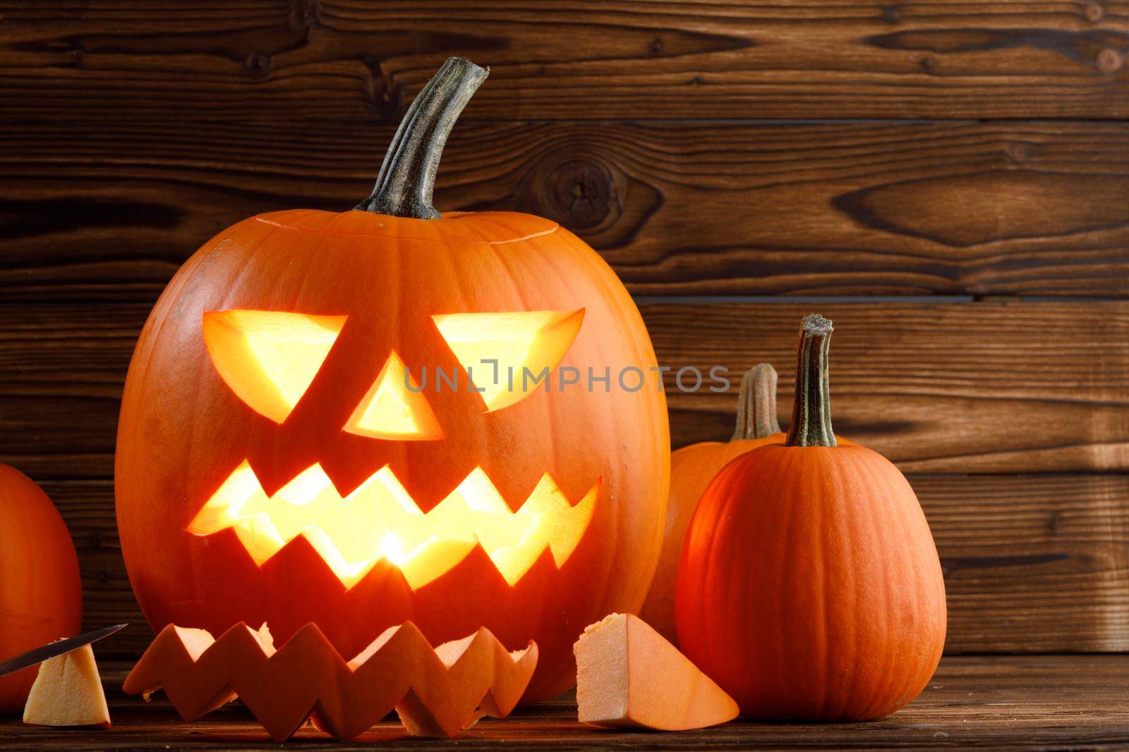 Carved halloween pumpkin with burning candle inside on wooden backdrop