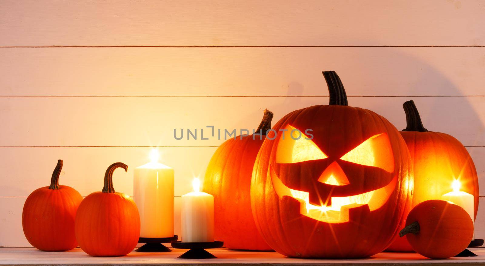 Glowing carved Halloween pumpkins head jack lantern and burning candles on light wooden background