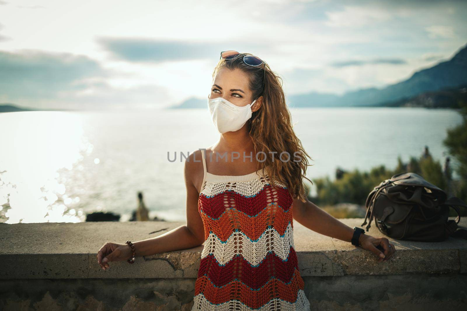 Shot of a happy young woman with protective mask spending time on seaside during exploring a Mediterranean at corona pandemic. 