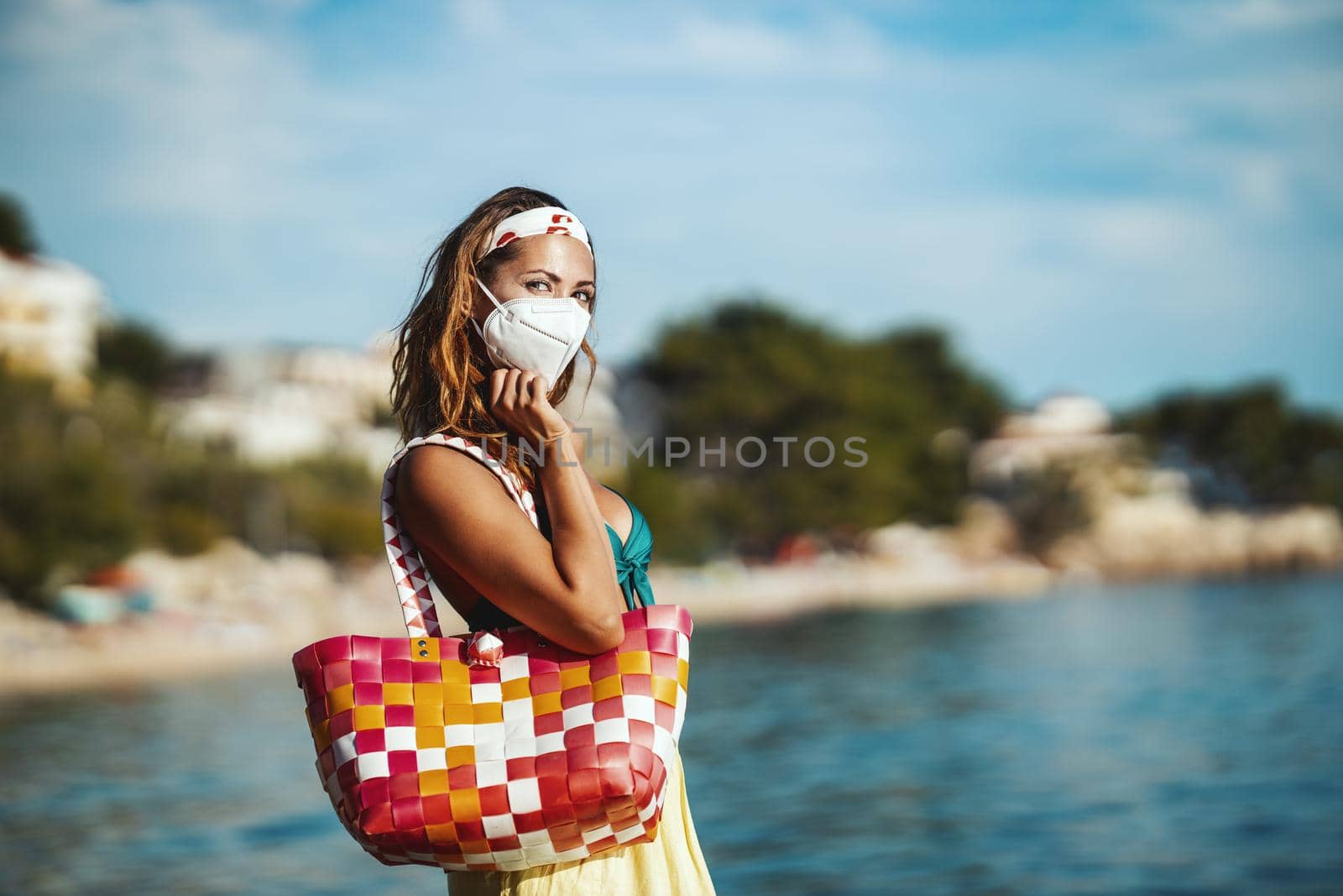 Shot of an attractive young woman in bikini with surgical mask enjoying a vacation on the beach during the COVID-19.