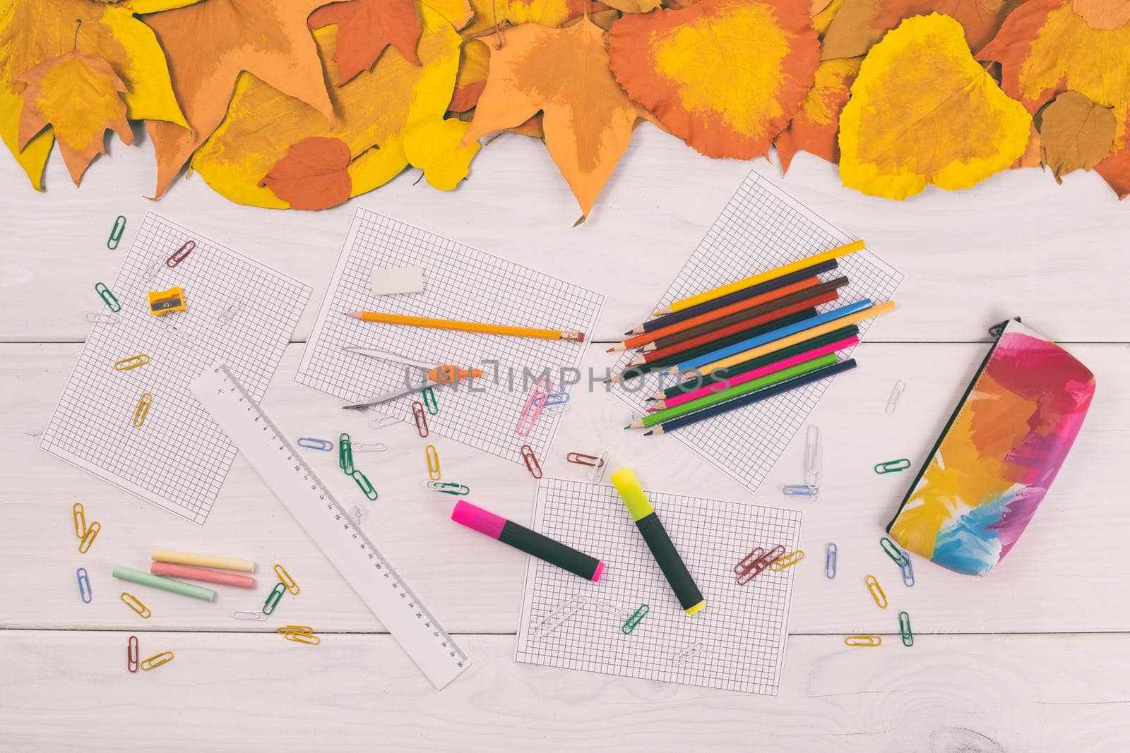 Empty white papers and school supplies on wooden table with painted leaves.Toned image.