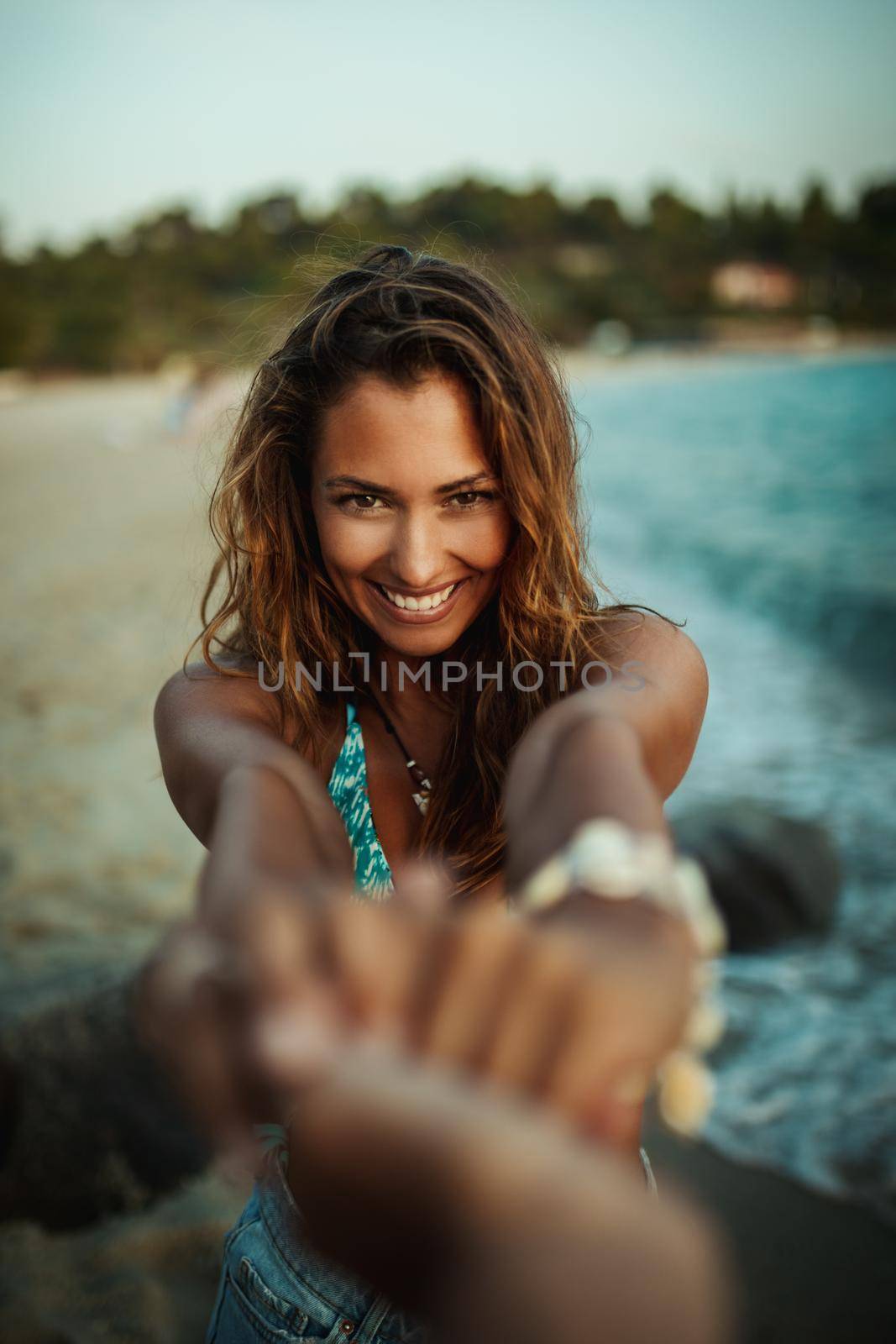 Shot of an attractive young woman leading someone by the hand at the beach.