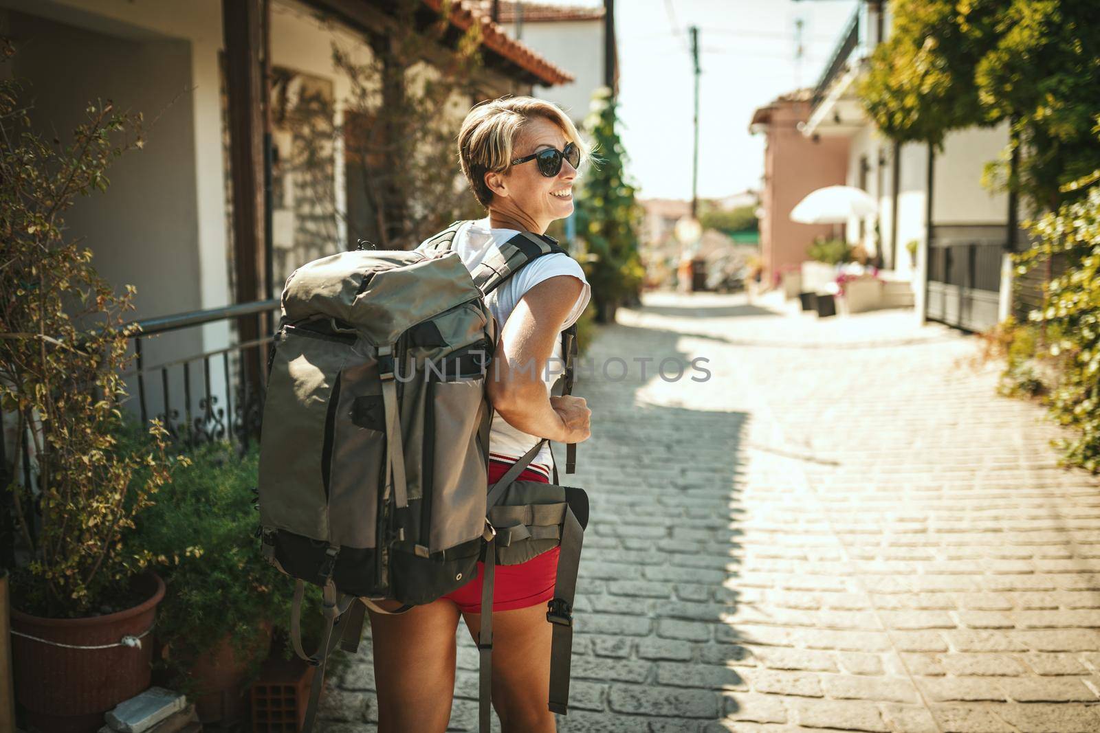 A beautiful young tourist arrived in a Mediterranean city with a backpack on her back. She is enjoying in summer sunny day.