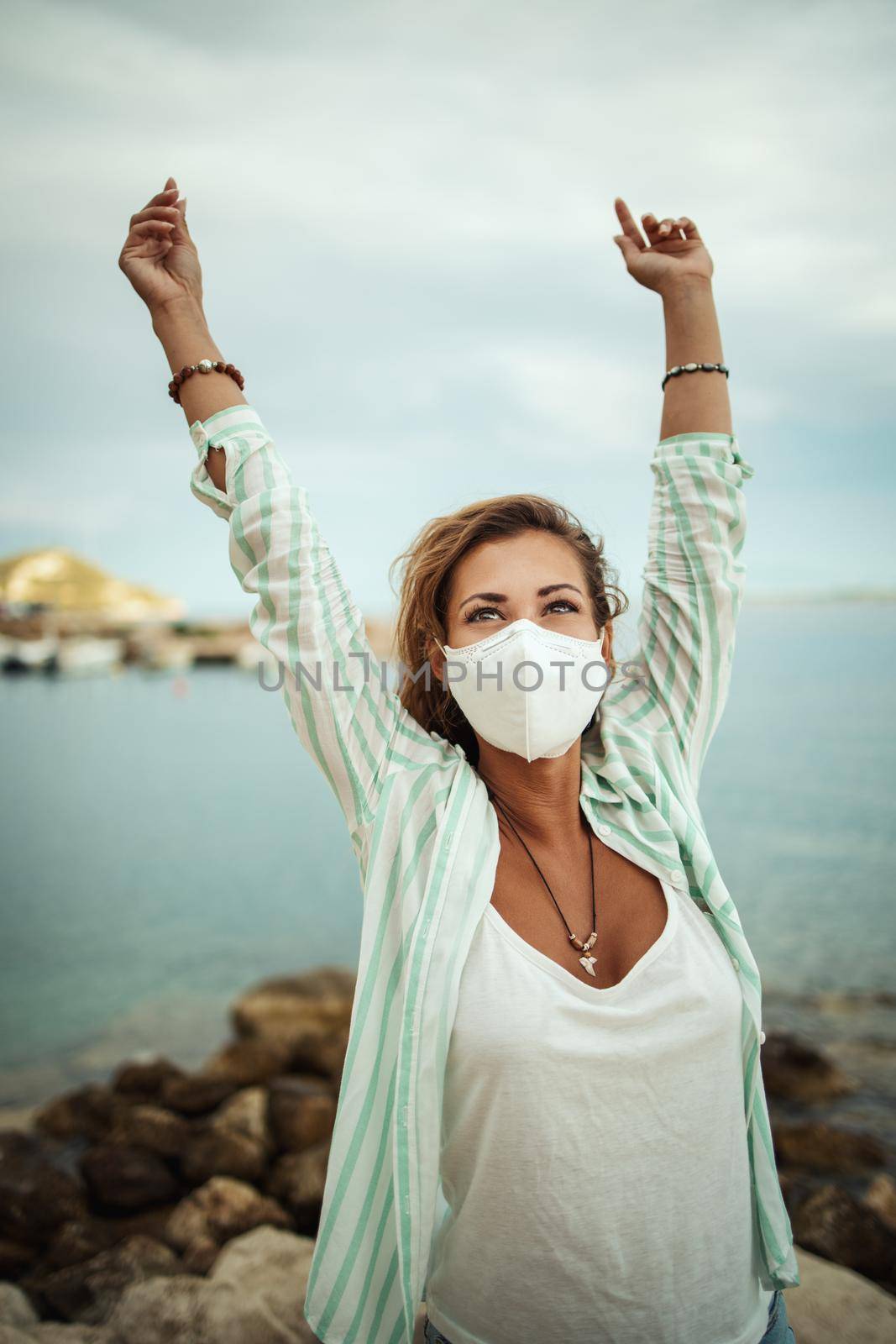 Shot of a happy young woman with protective N95 mask enjoying while spending time on the seaside during the COVID-19.