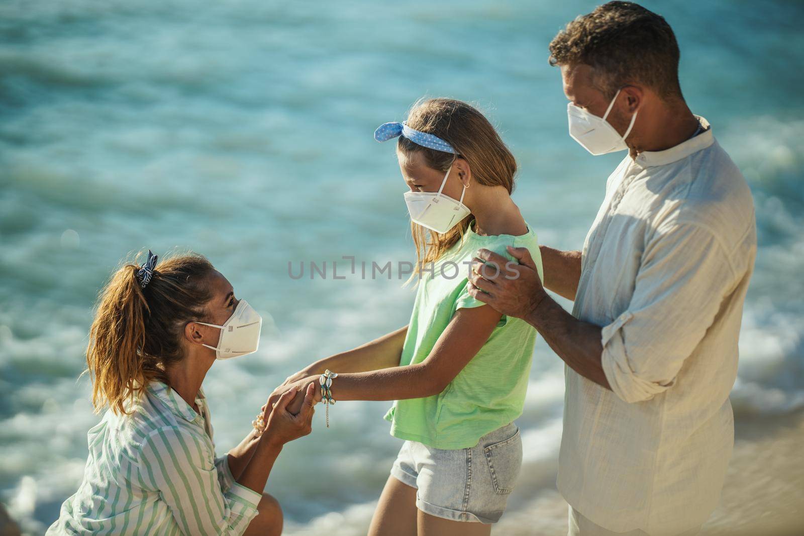 Shot of a happy family with protective N95 mask spending time on the seashore at corona pandemic. 
