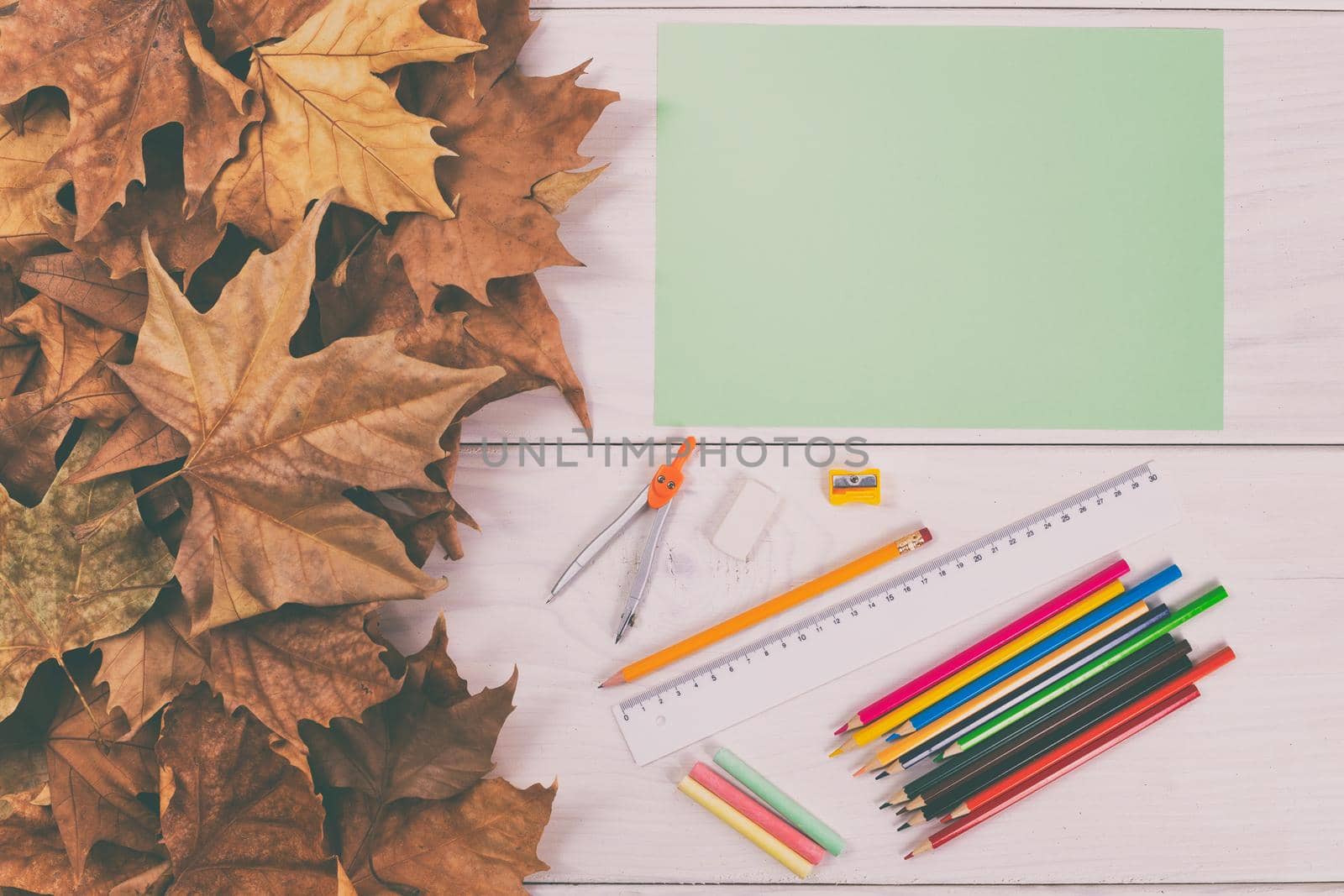 Empty green paper and school supplies on wooden table with autumn leaves by Bazdar