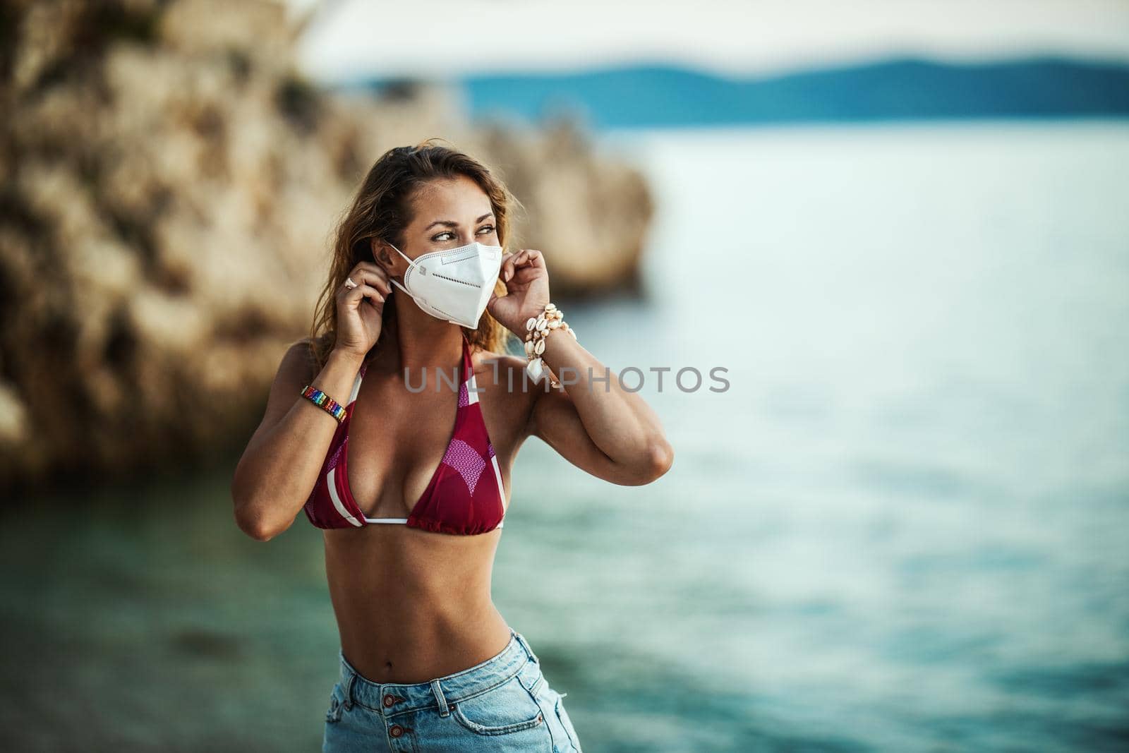 Shot of an attractive happy young woman with surgical mask enjoying a vacation on the beach during the COVID-19.