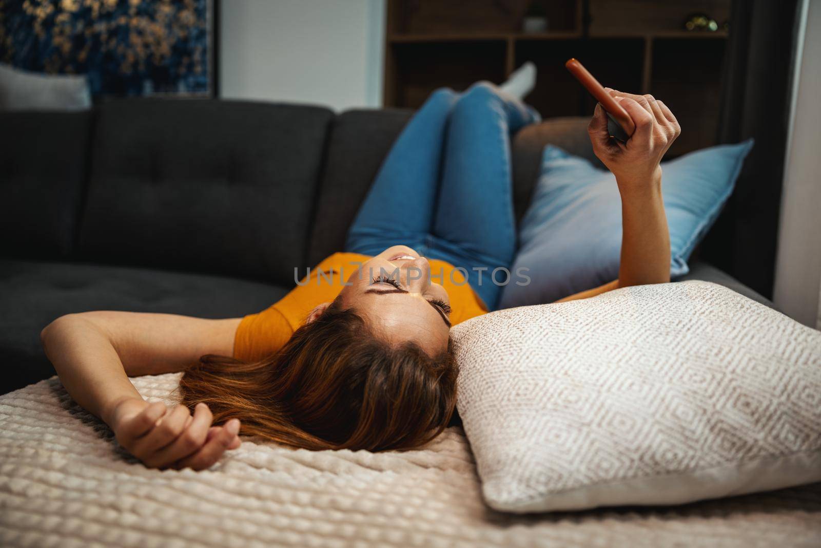 Attractive young woman lying on the sofa and using smartphone to surfing sthe net at home.