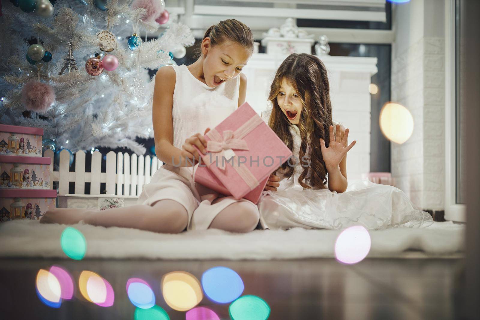 Shot of a two excited little girls opening their Christmas gifts by a white Christmas tree at the home.