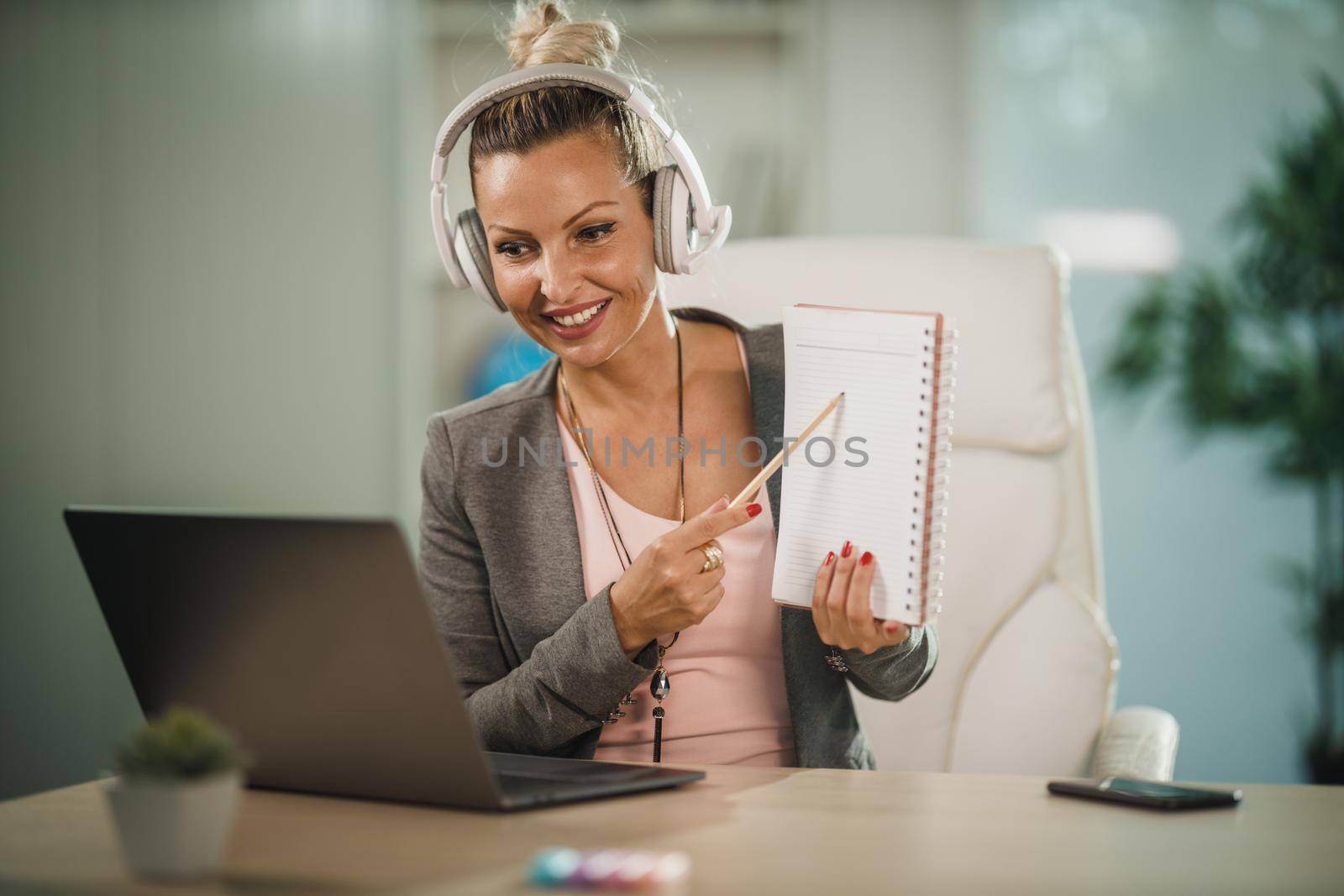 Shot of a attractive young businesswoman sitting alone in her home office with headphones and working on laptop during COVID-19 pandemic.