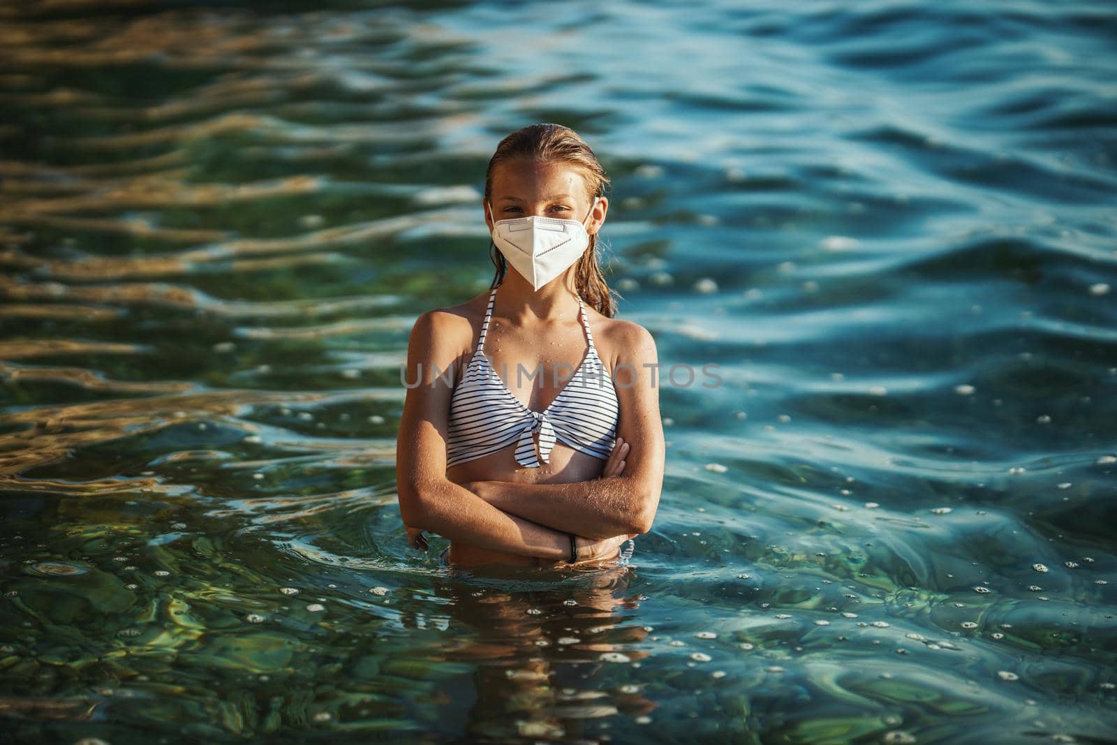 Shot of an happy teenager wearing surgical mask enjoying a vacation on the beach during the COVID-19. Looking at camera.