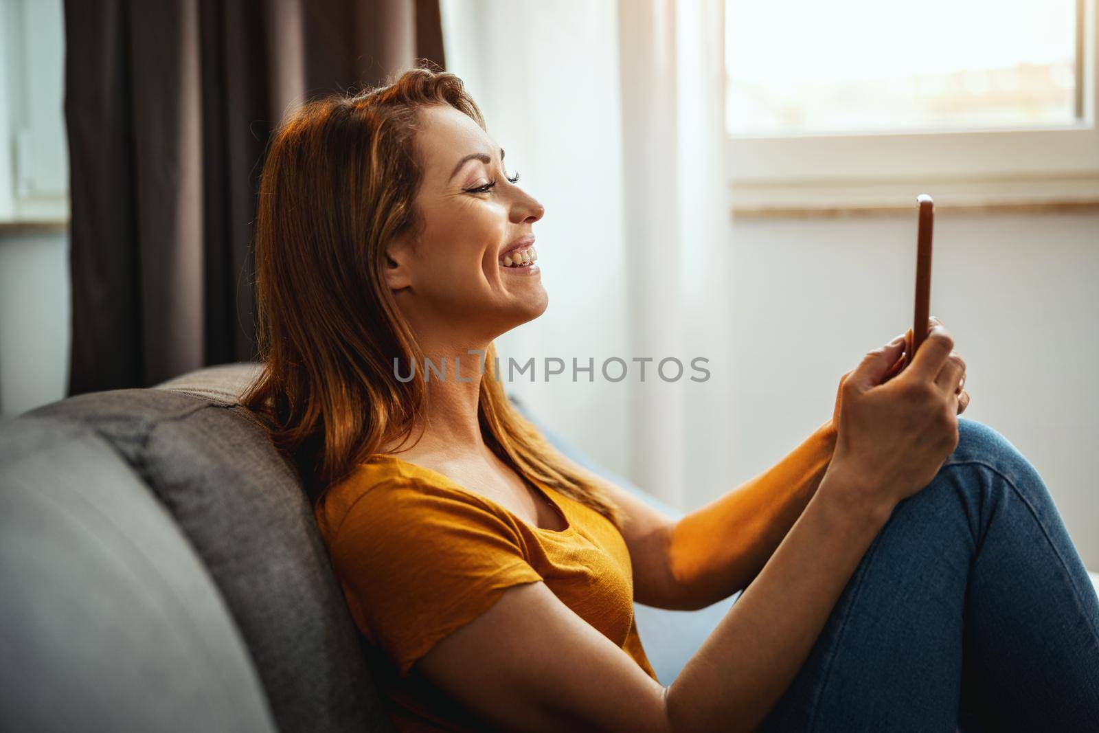 Attractive young woman sitting on the sofa and using smartphone to making video chat at home.