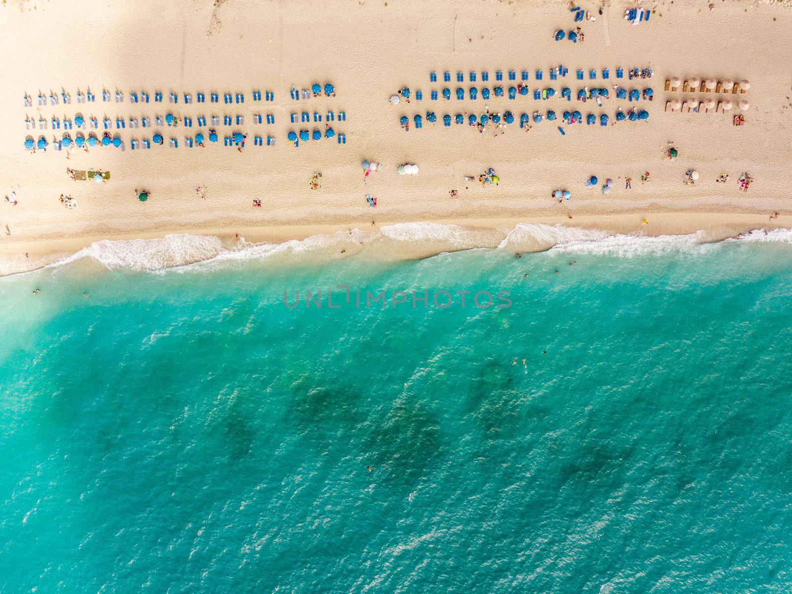 Aerial view from drone of sandy beach with tourists relaxing next to clear water of Mediterranean sea at sunny day.