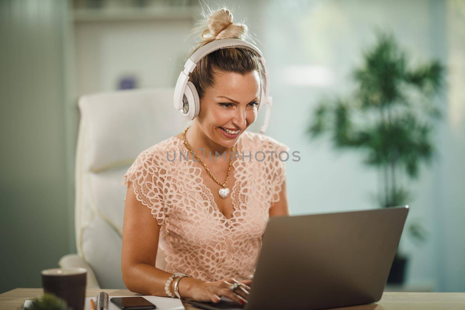 Shot of a attractive young businesswoman sitting alone in her home office with headphones and working on laptop during COVID-19 pandemic.