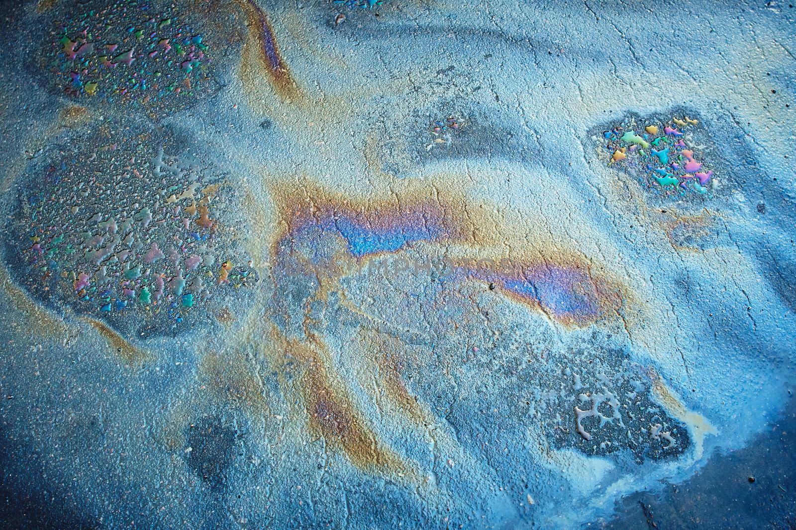 Oil stain on Asphalt road after rain. Multi-colored poisonous spots on the parking. Multi-colored oil stain on the pavement.