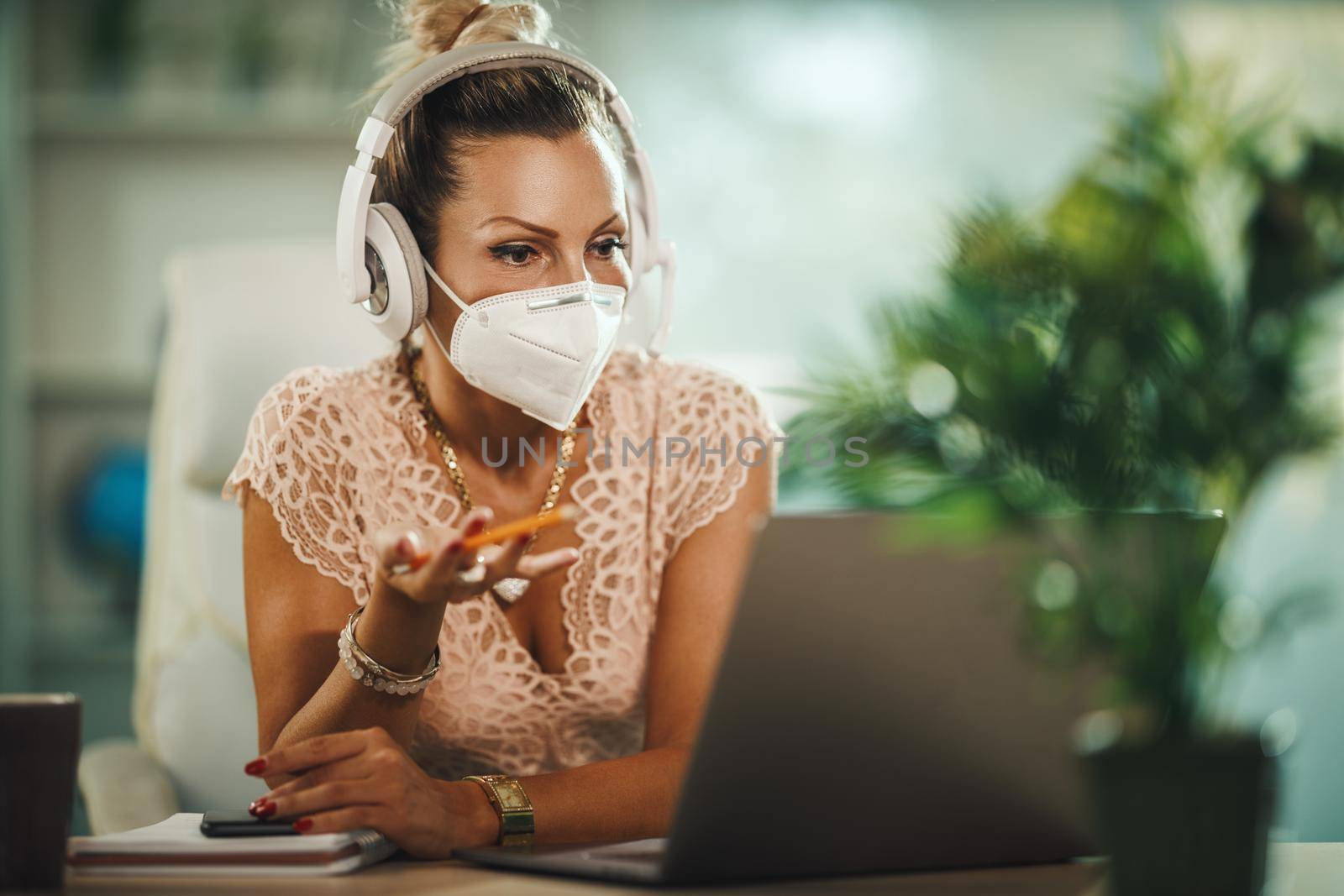 Shot of a attractive young businesswoman with N95 protective mask sitting alone in her home office and making video call on her laptop during COVID-19 pandemic.