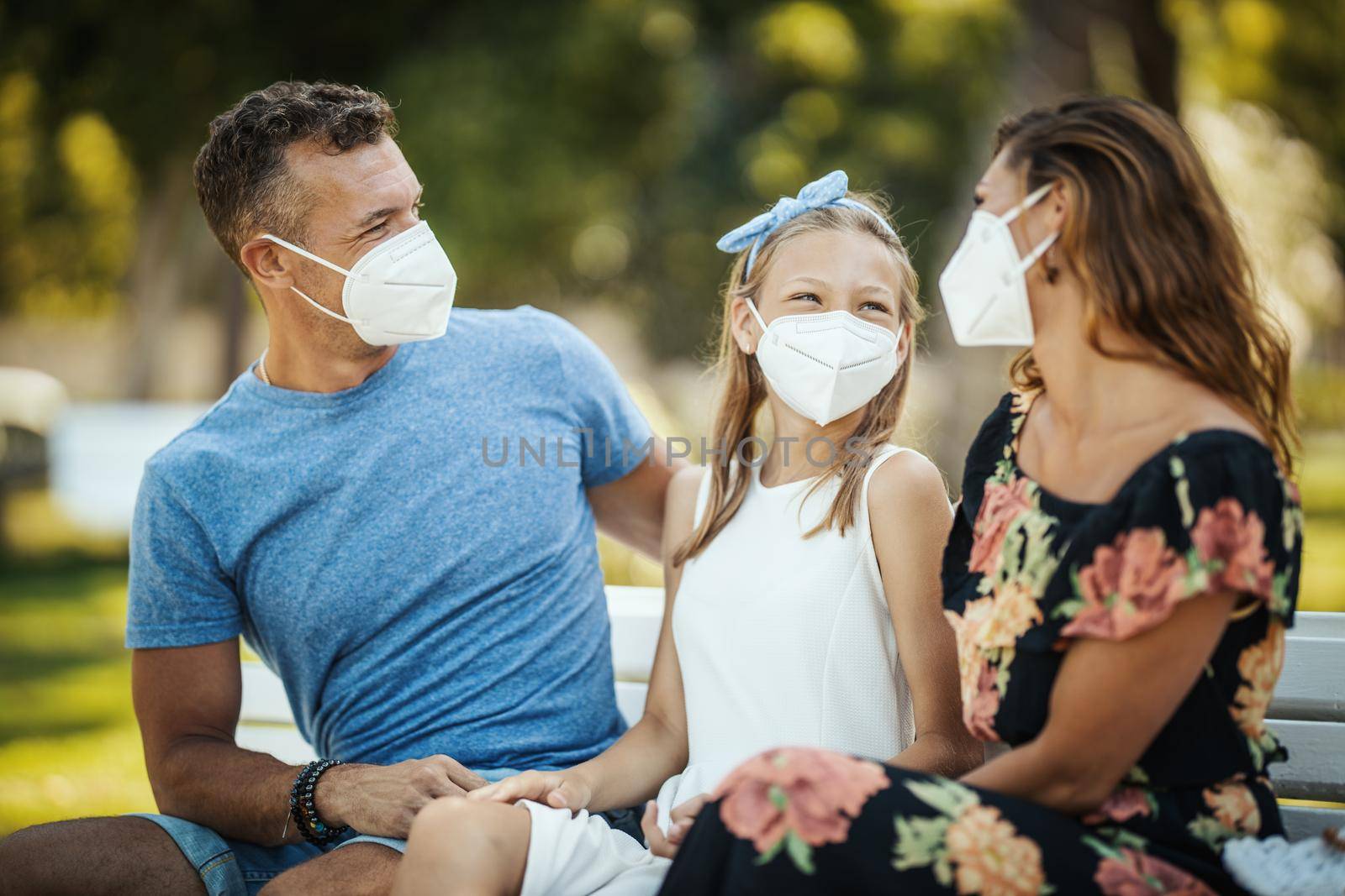 Self-isolation in nature. Young happy family with protective N95 mask having fun during spending time in the park at corona pandemic.