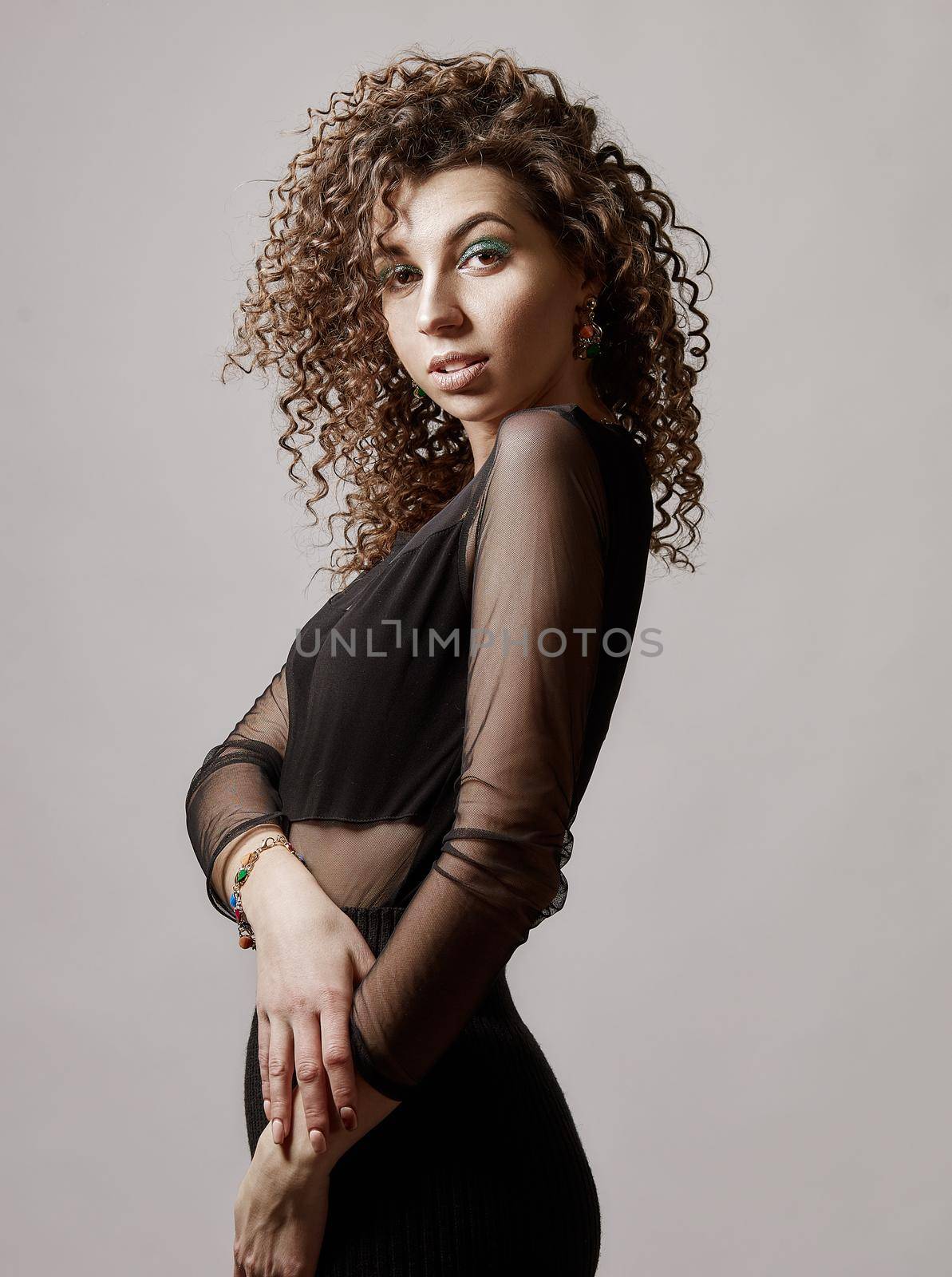 Happy mixed race girl with curly hair is hugging herself, standing on grey background