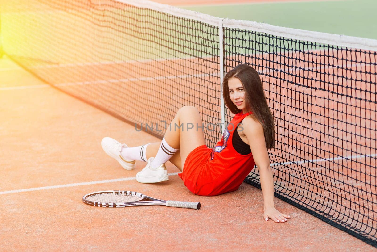 Beautiful female tennis player on tennis court in red dress.