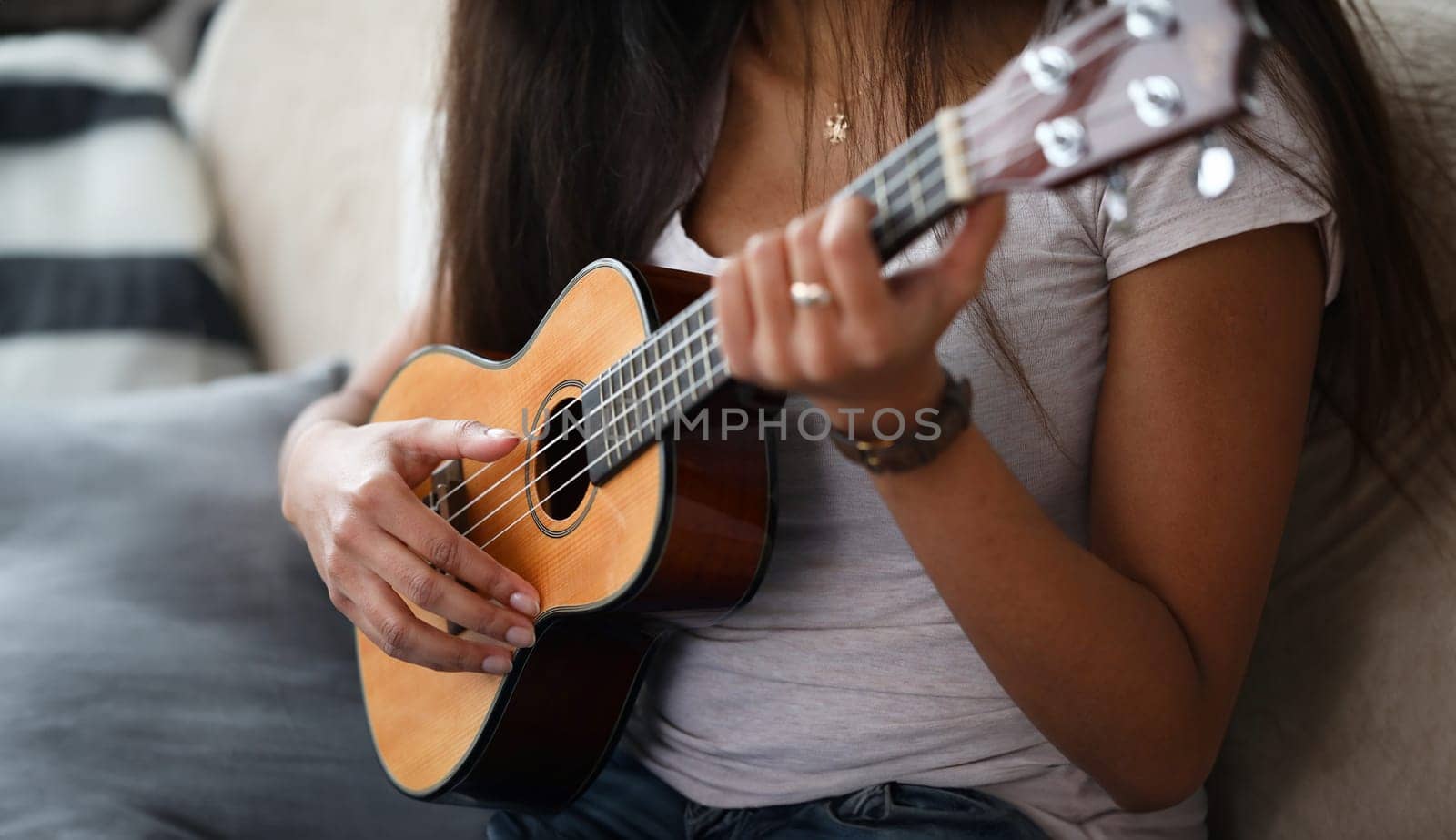 Close-up of latino woman holding ukulele and learning how to play. Young female exercising in playing. Musical wooden instrument. Music and art concept