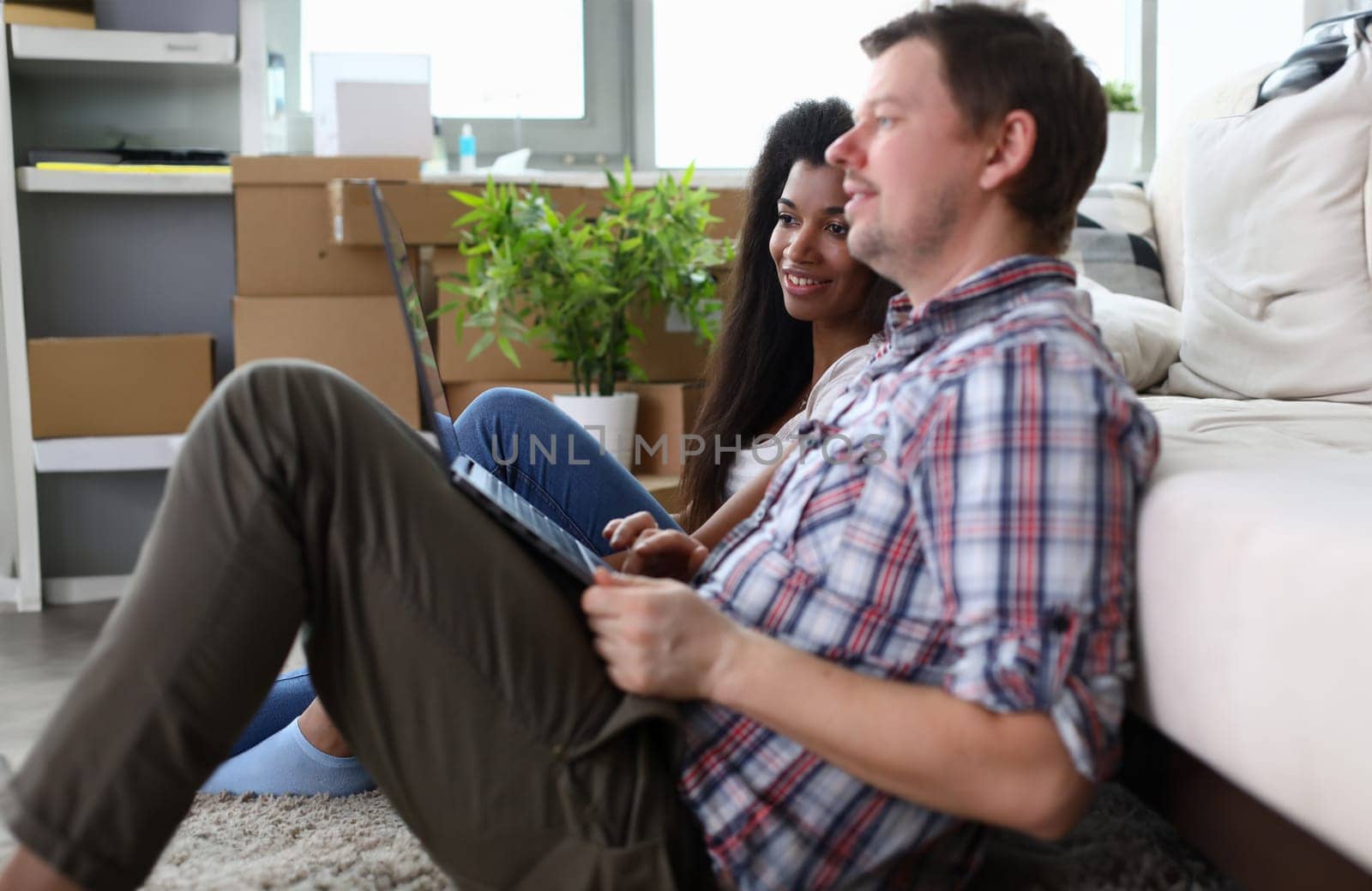 Portrait of man and latino woman watching design advices on portable computer. Wife and husband dreaming about something and smiling. Relocation and renovation concept