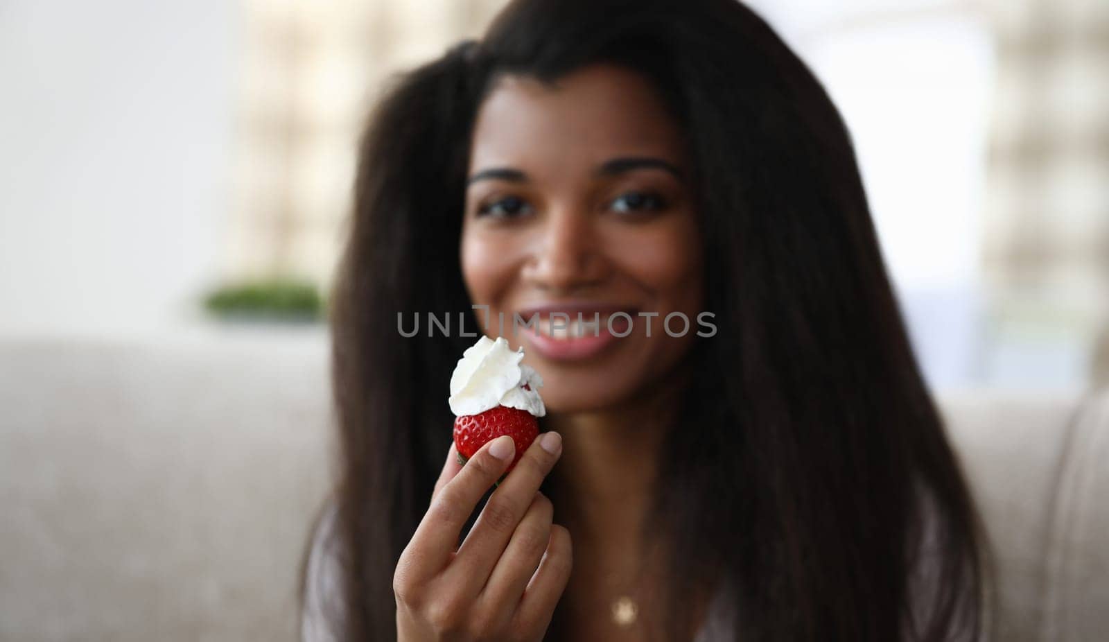 Close-up of african-american young woman holding strawberry with whipped cream by kuprevich