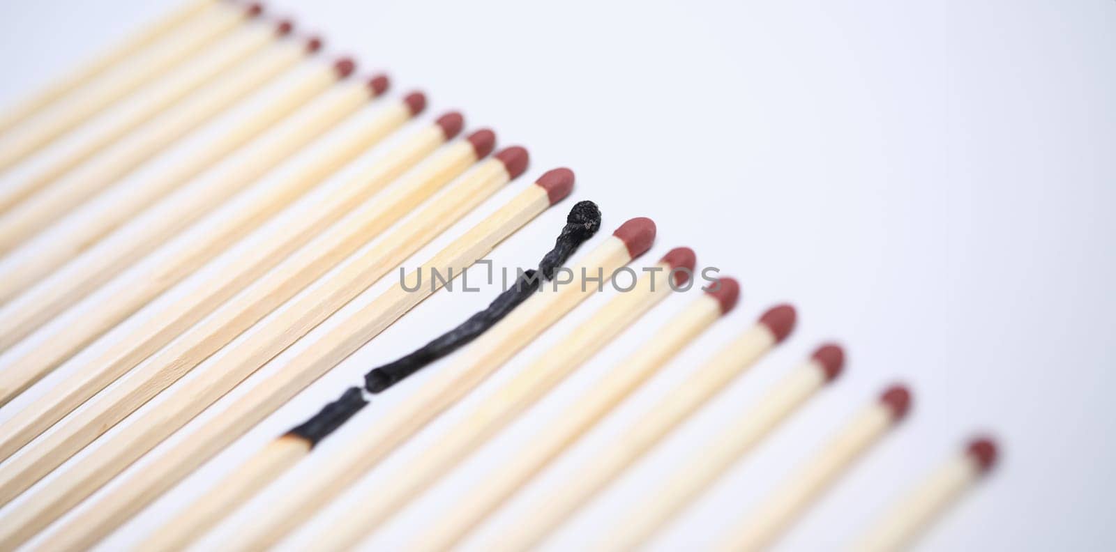 Close-up view of one wooden burnt match among many new whole. Conceptual image of non-renewable energy. Burn out syndrome and stress concept. Isolated on white background