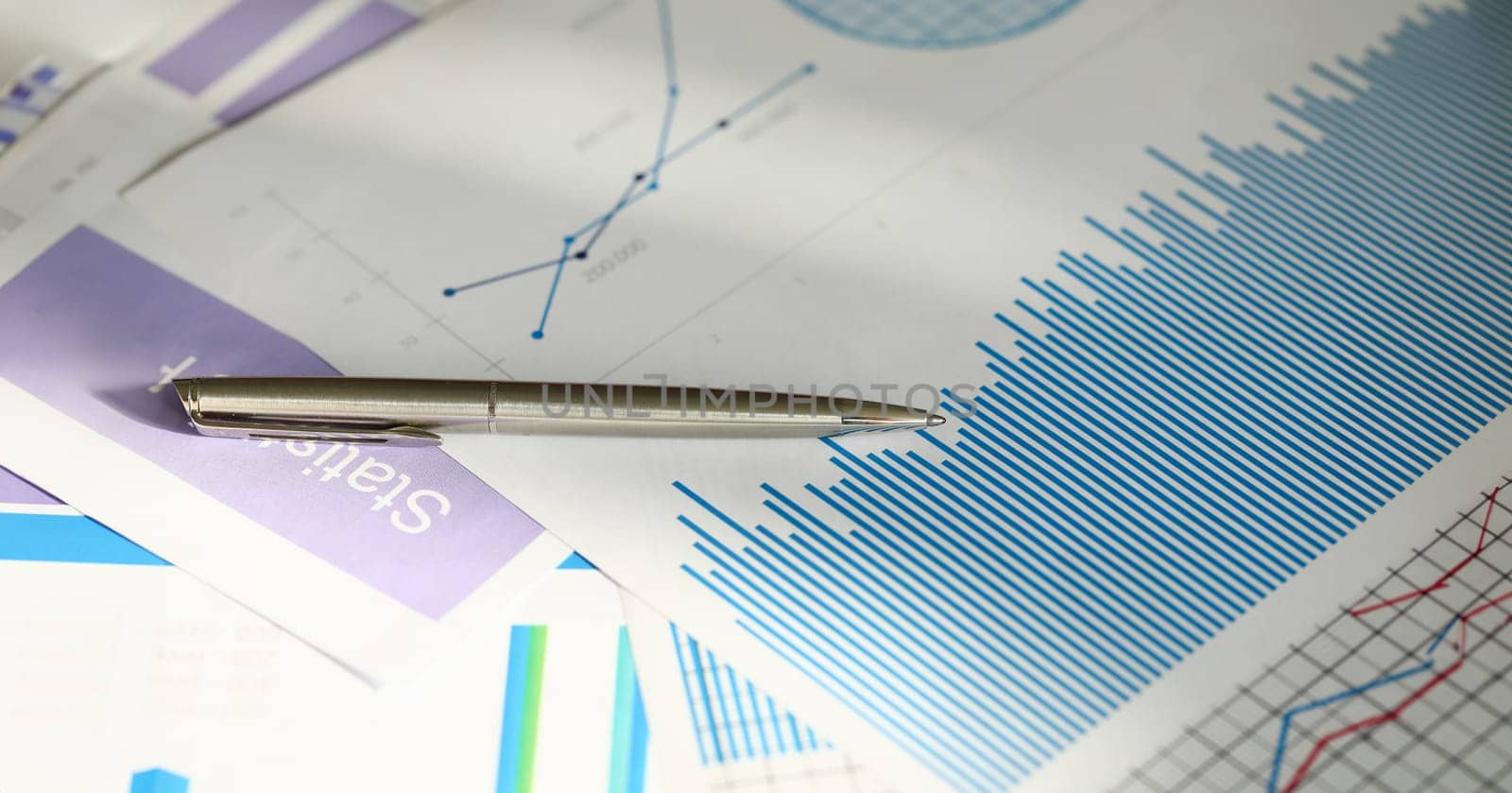 Close-up of analysis graphics on table with silver pen. Important documentation with colourful charts and graphs. Finance report accounting statistics business concept