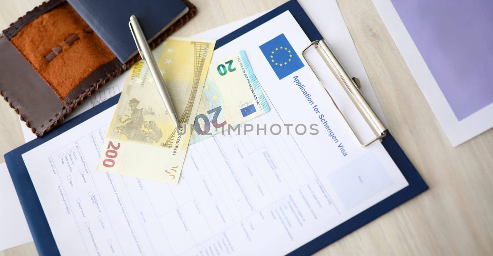 Close-up of clipboard with application for schengen visa document. Passport and paper banknotes on table. Form for personal information. European union and travelling abroad concept