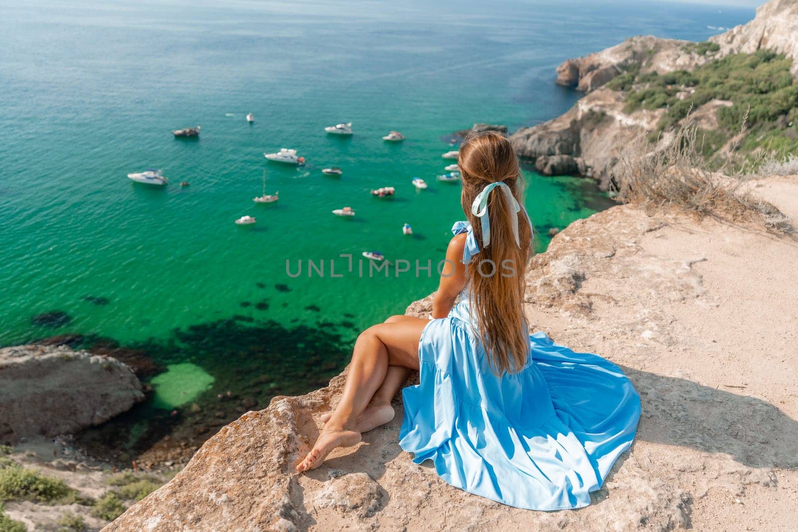 Woman travel sea. Happy woman in a beautiful location poses on a cliff high above the sea, with emerald waters and yachts in the background, while sharing her travel experiences.