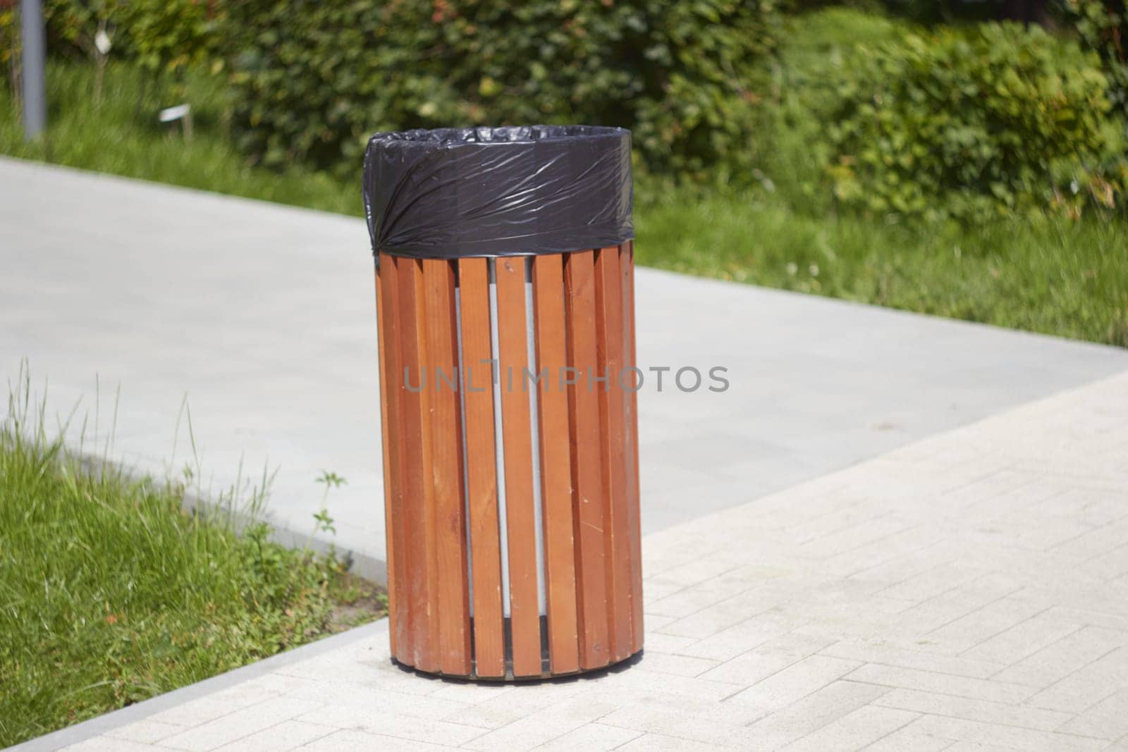 Photo of slatted wastebasket at intersection of footpaths. Cleaning of parks and squares of city.
