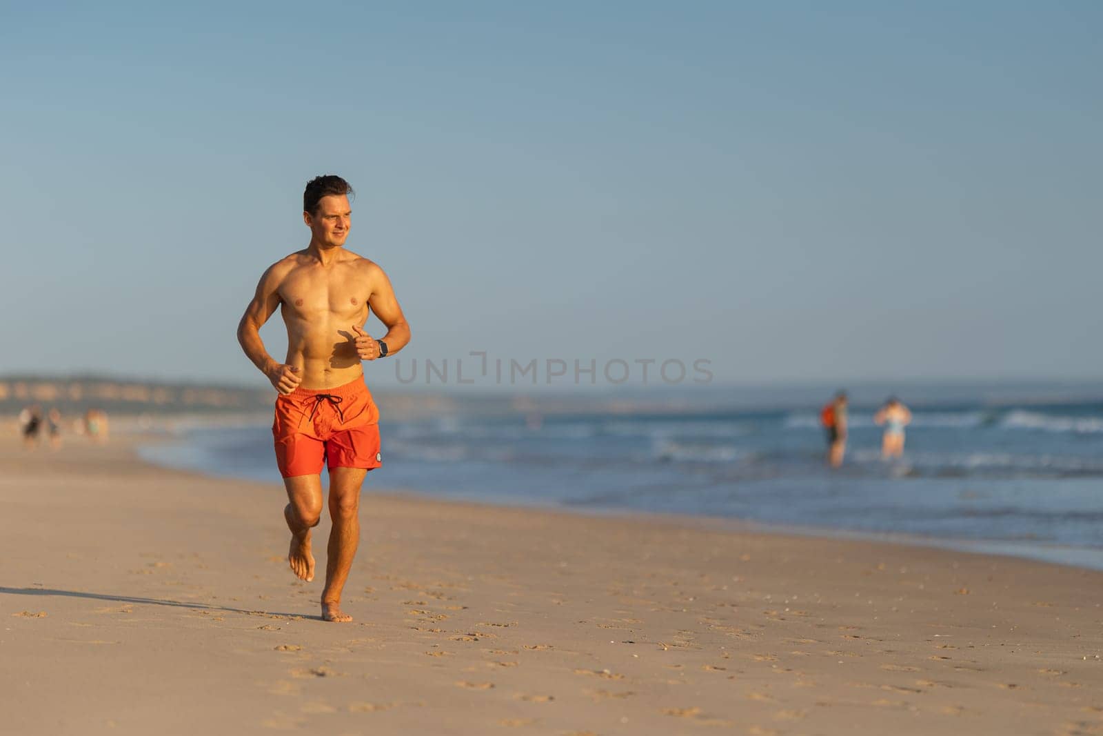 An attractive man with nice athletic body jogging on the shore. Mid shot