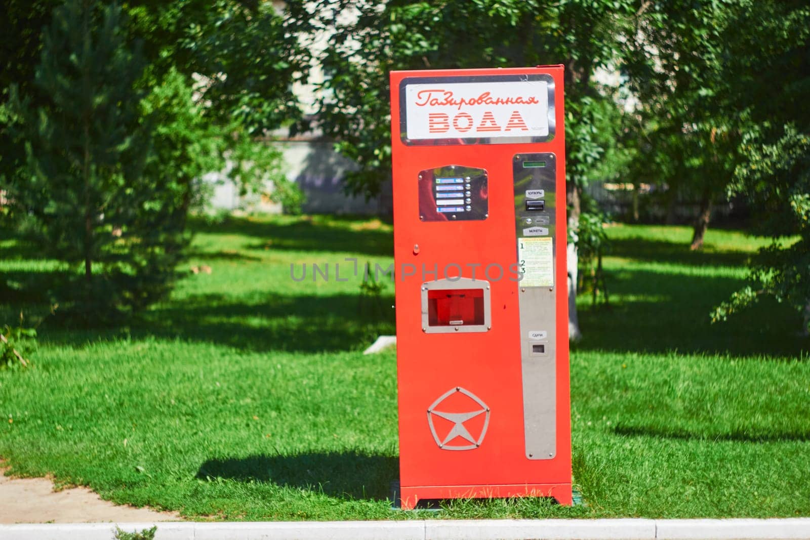 Photo red modern apparatus for soft drinks carbonated water. In practice against backdrop of green trees.