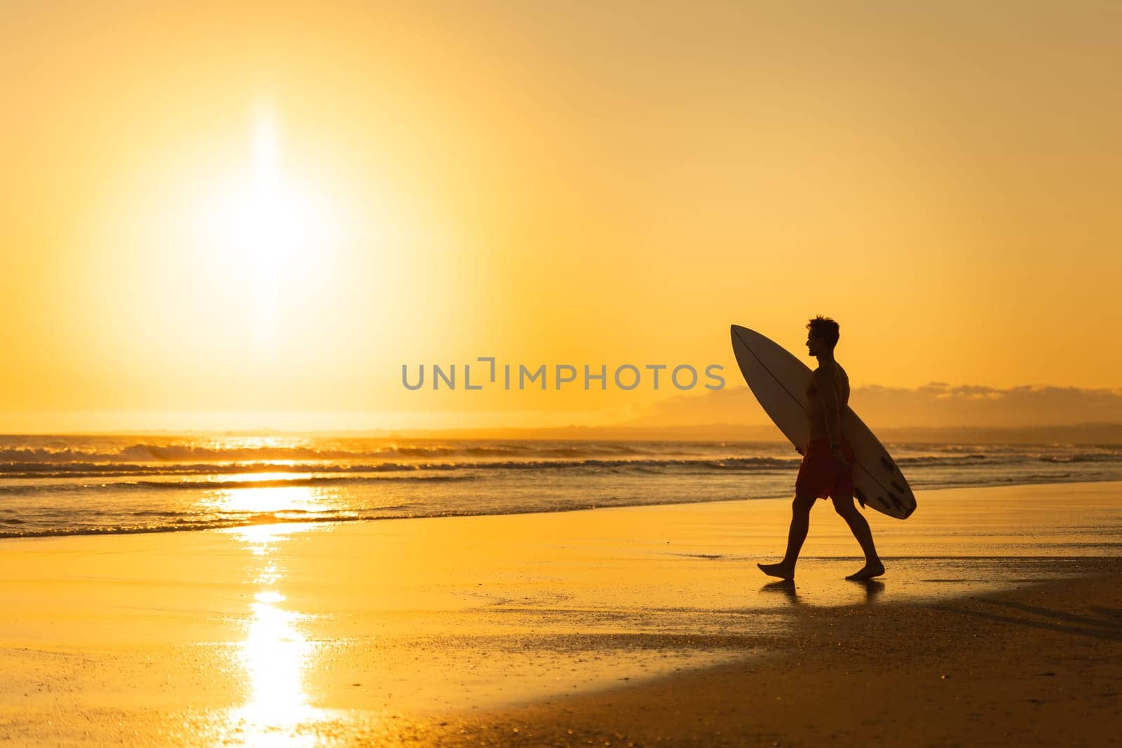Silhouette of a man walking to the ocean at bright sunset. Mid shot