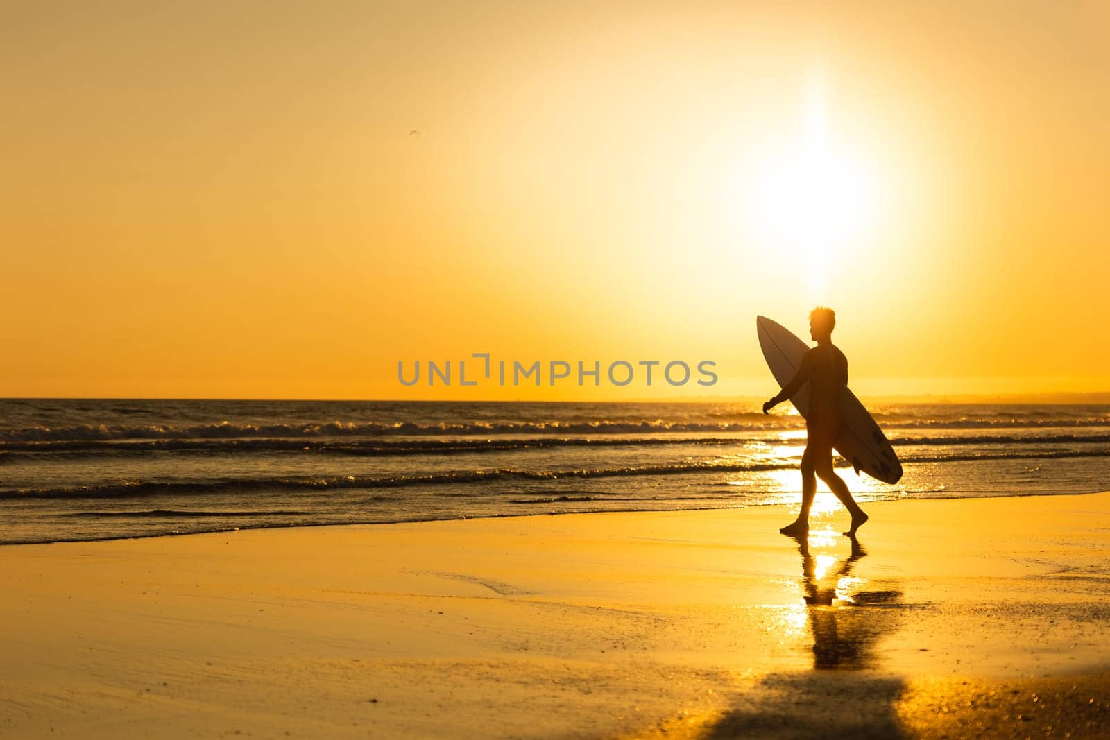 Silhouette of a man walking to the ocean at bright late sunset. Mid shot