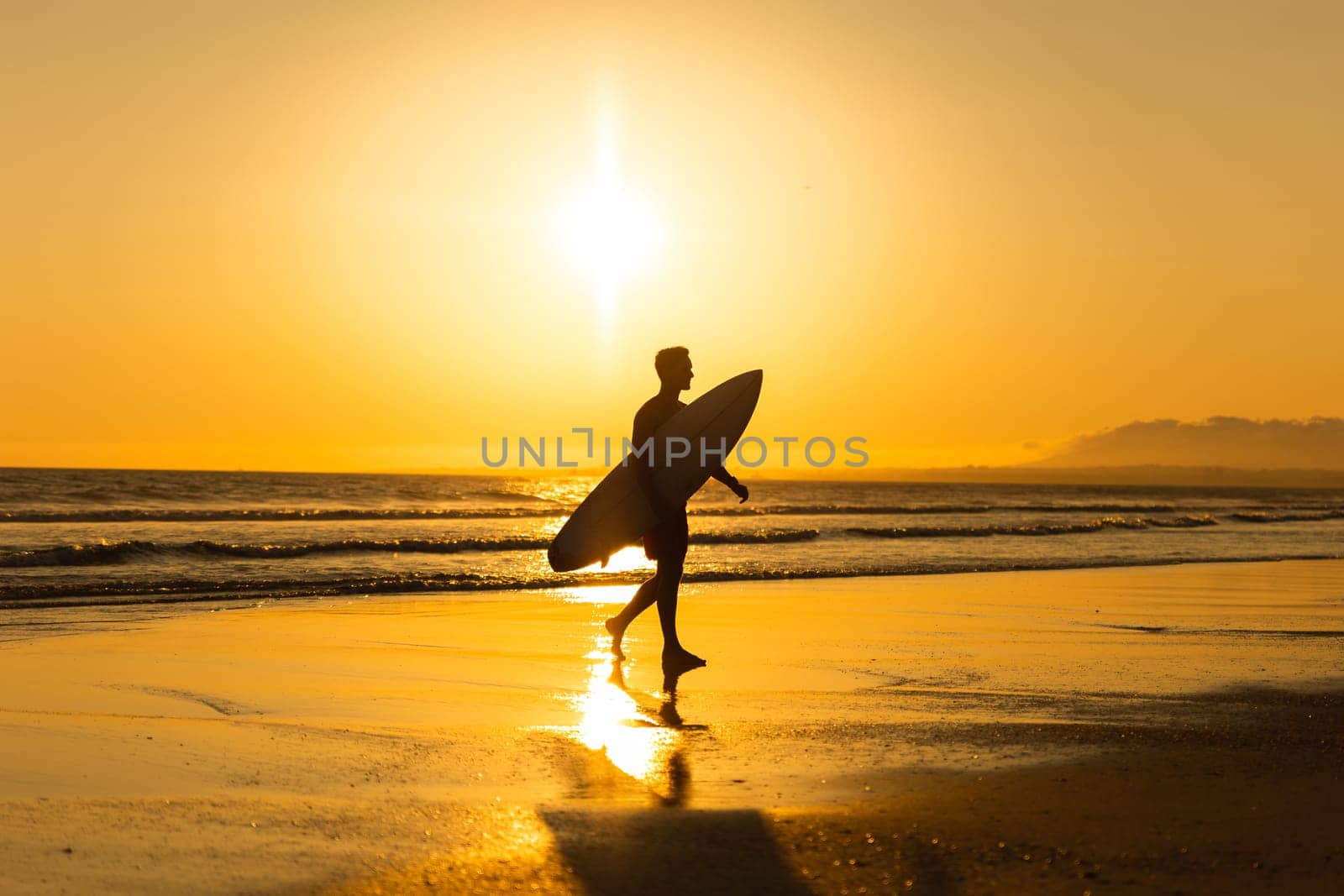 Silhouette of a man walking out of the ocean at bright sunset. Mid shot