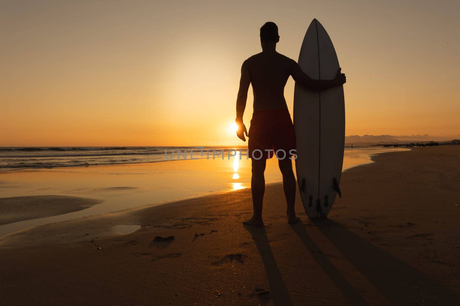 Black silhouette of a man standing on the shore at sunset. Mid shot