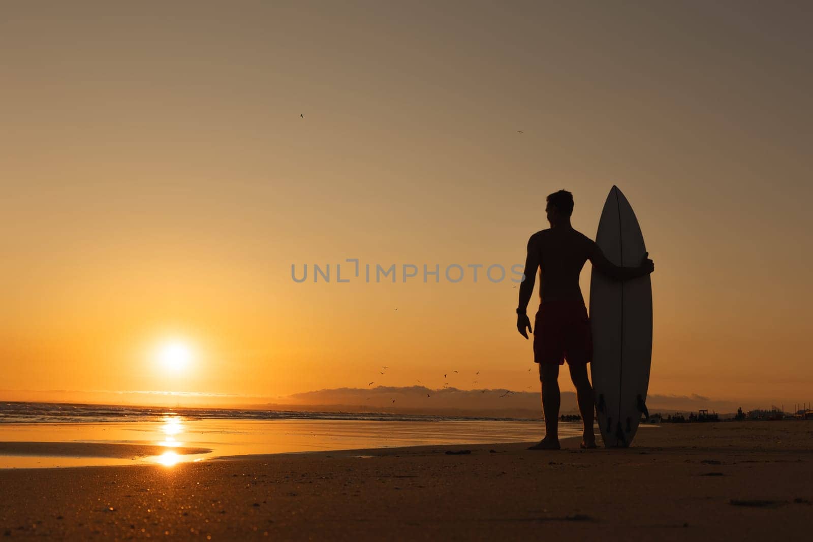Black silhouette of an athletic man standing on the shore at sunset. Mid shot