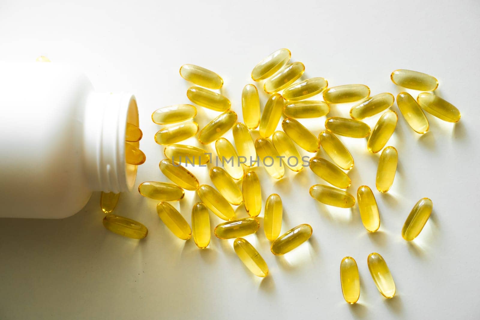 Open bottle with omega-3 capsules. Next to the lid with capsules. Medical concept. Pile of yellow softgel capsules Omega 3 fish oil scuttered from a white bottle bottle. Health care concept. by vovsht