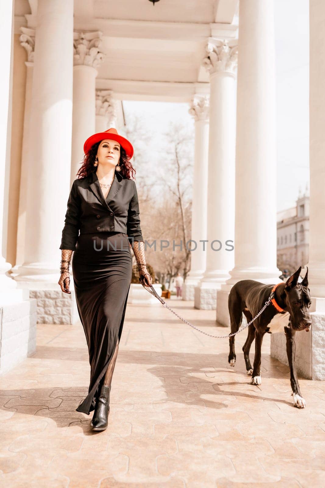 A photo of a woman and her Great Dane walking through a town, taking in the sights and sounds of the urban environment.