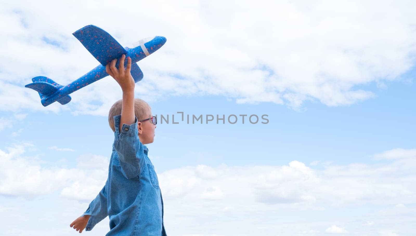 Rear view of a child boy with an airplane dreams of traveling in the summer in nature against the blue sky.