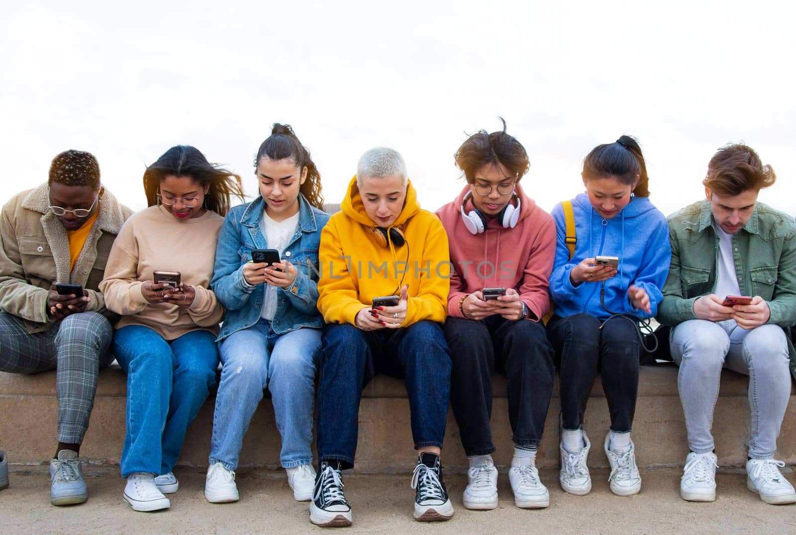 Multiracial group of teen college students ignoring each other looking at mobile phone checking social media. by Hoverstock