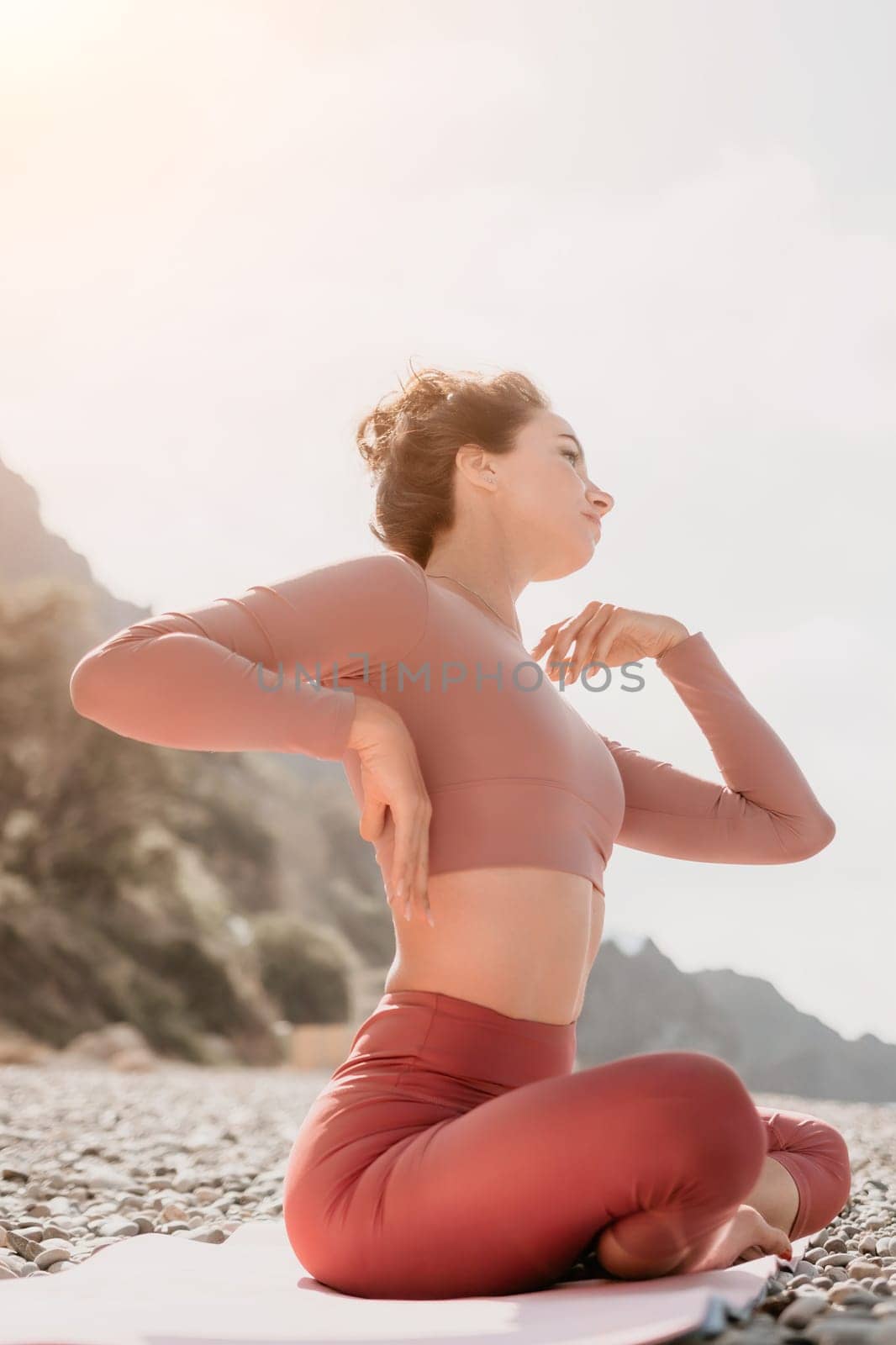 Middle aged well looking woman with black hair, fitness instructor in leggings and tops doing stretching and pilates on yoga mat near the sea. Female fitness yoga routine concept. Healthy lifestyle by panophotograph