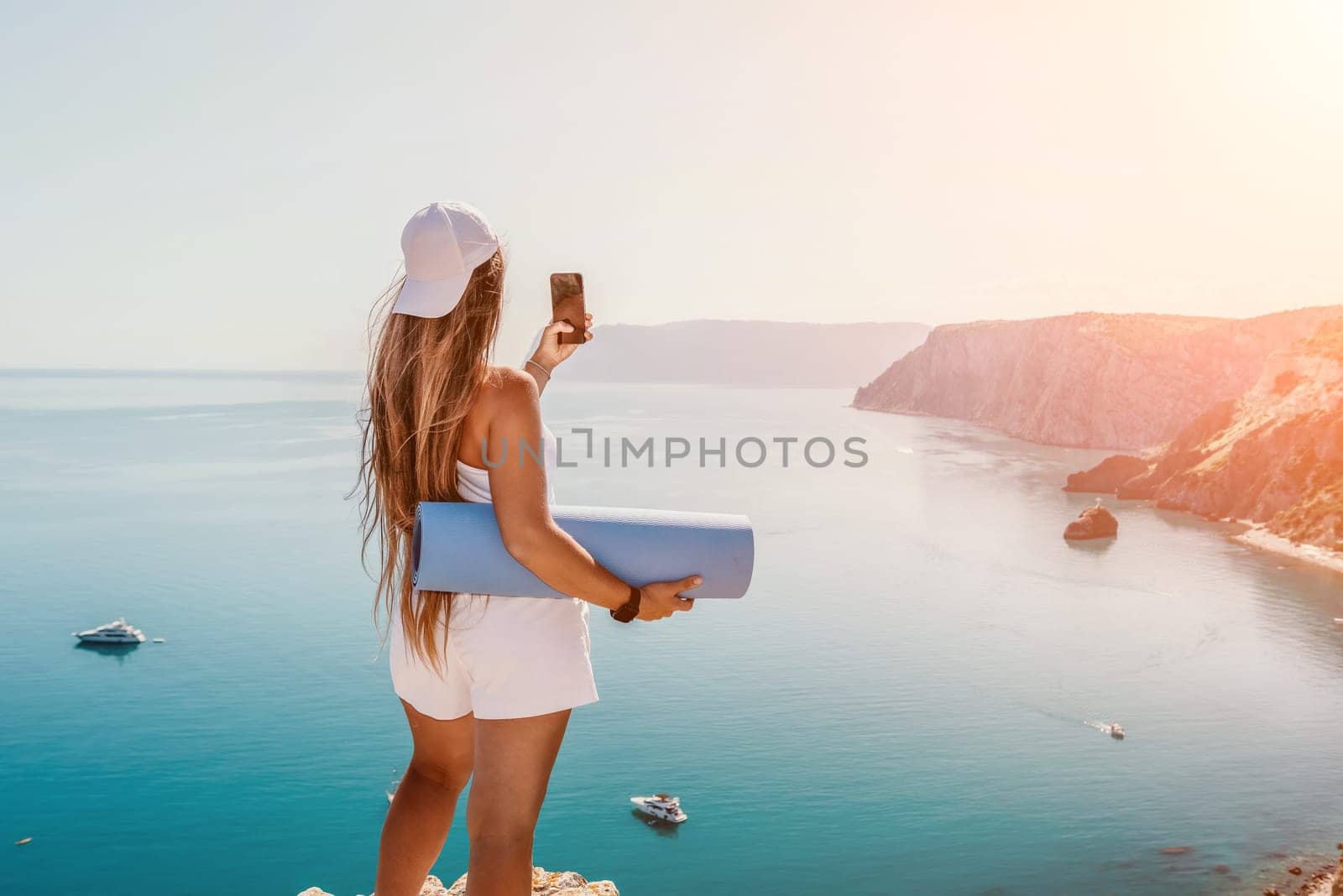 Woman with yoga mat over calm azure sea. Well looking middle aged woman with long hair, fitness instructor with blue yoga mat near the sea. Female fitness yoga routine concept. Healthy lifestyle. by panophotograph