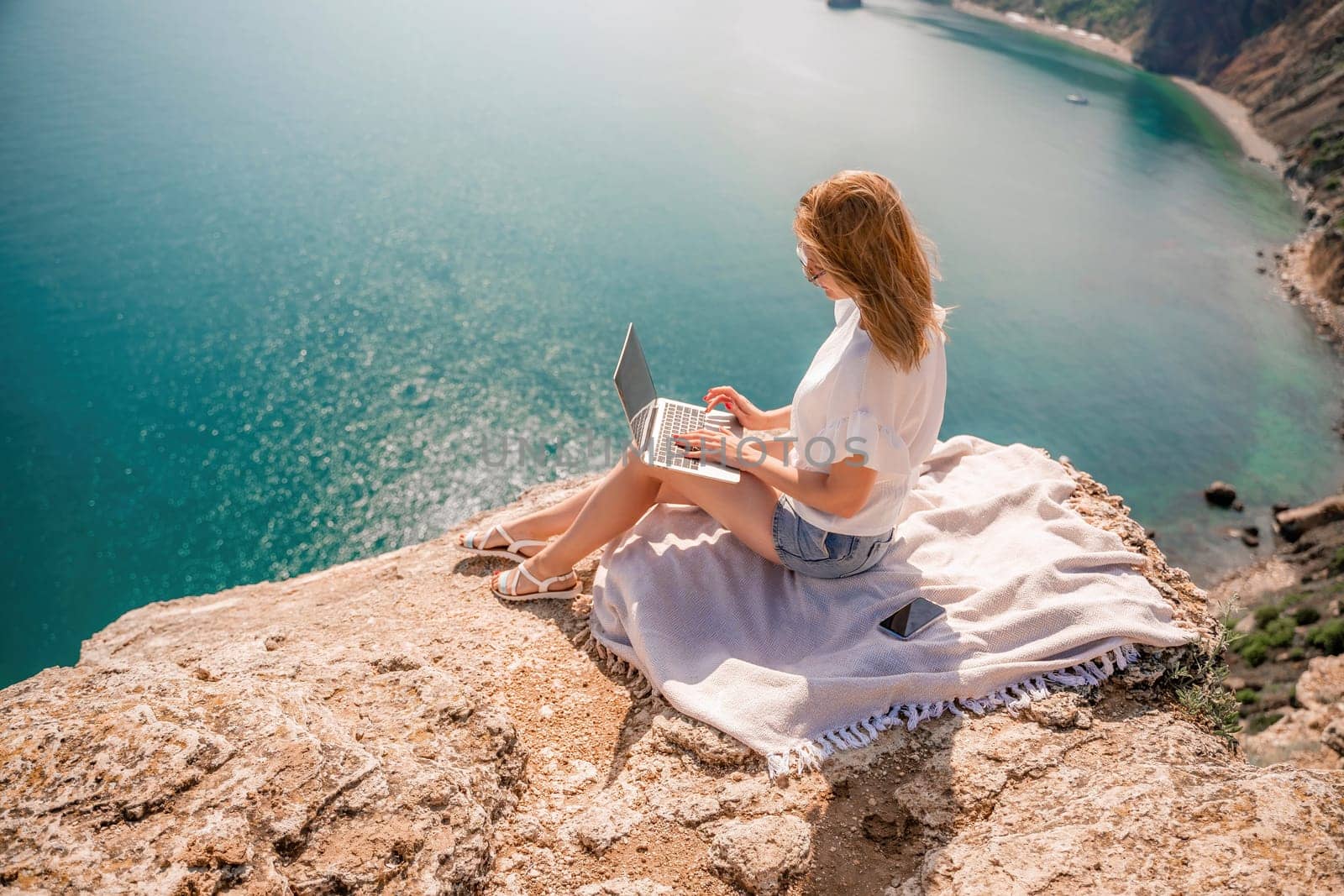 Freelance woman working on a laptop by the sea, typing away on the keyboard while enjoying the beautiful view, highlighting the idea of remote work