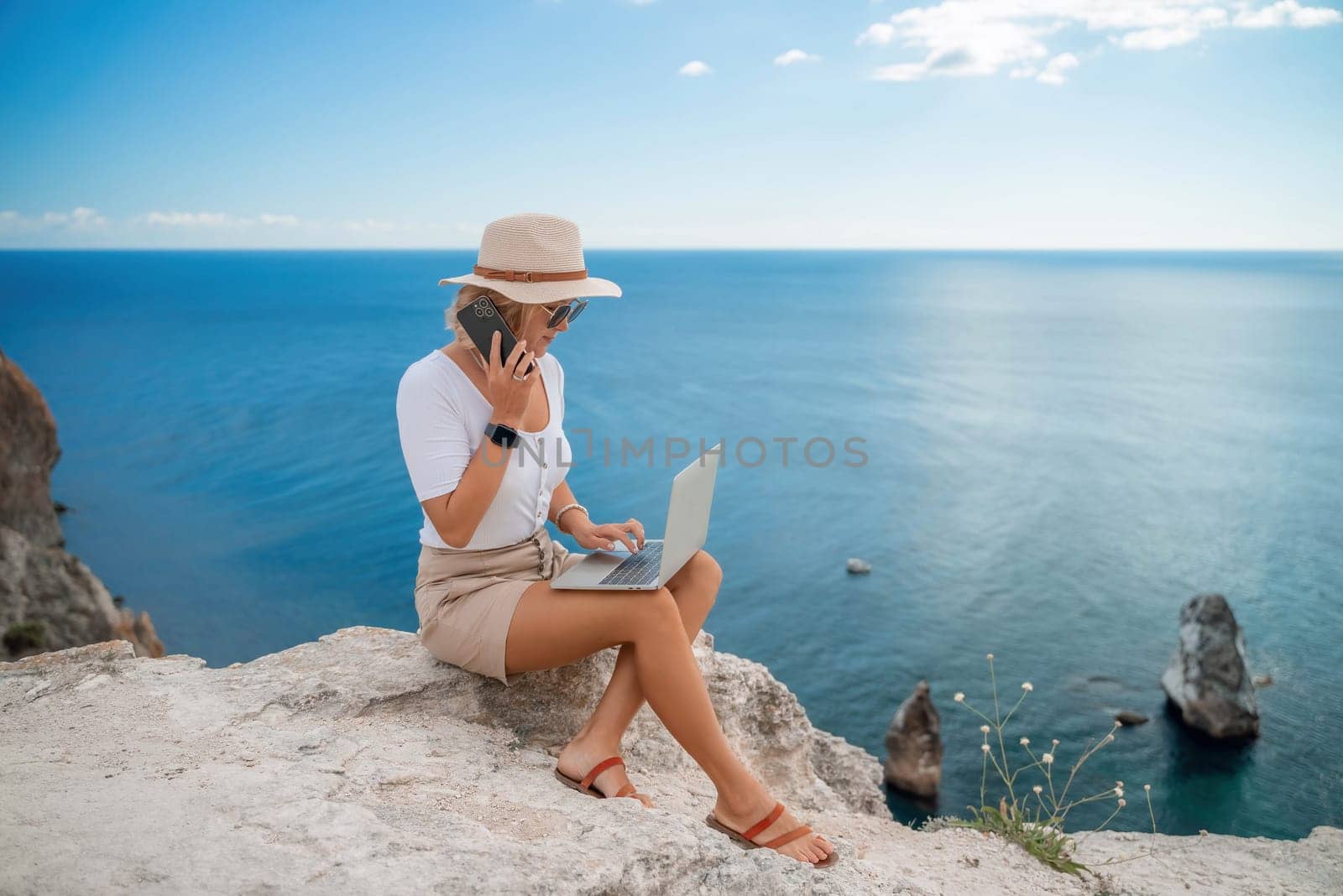 Freelance women sea working on the computer. Good looking middle aged woman typing on a laptop keyboard outdoors with a beautiful sea view. The concept of remote work